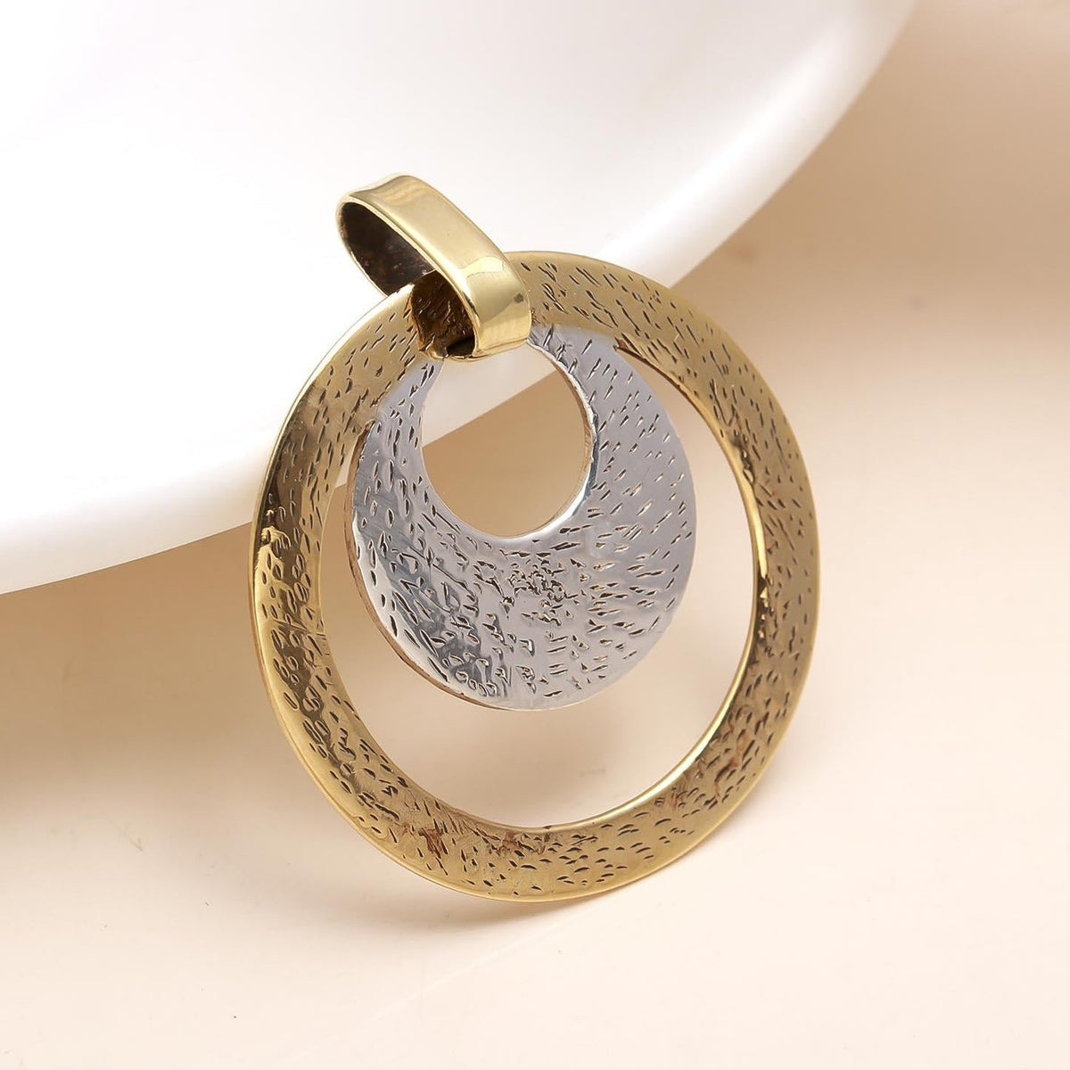 Gold and silver circular pendant on a beige background