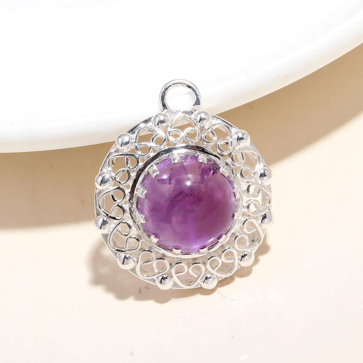 A round sterling silver pendant with a geometric pattern and a large purple gemstone in the center, placed on a white surface.