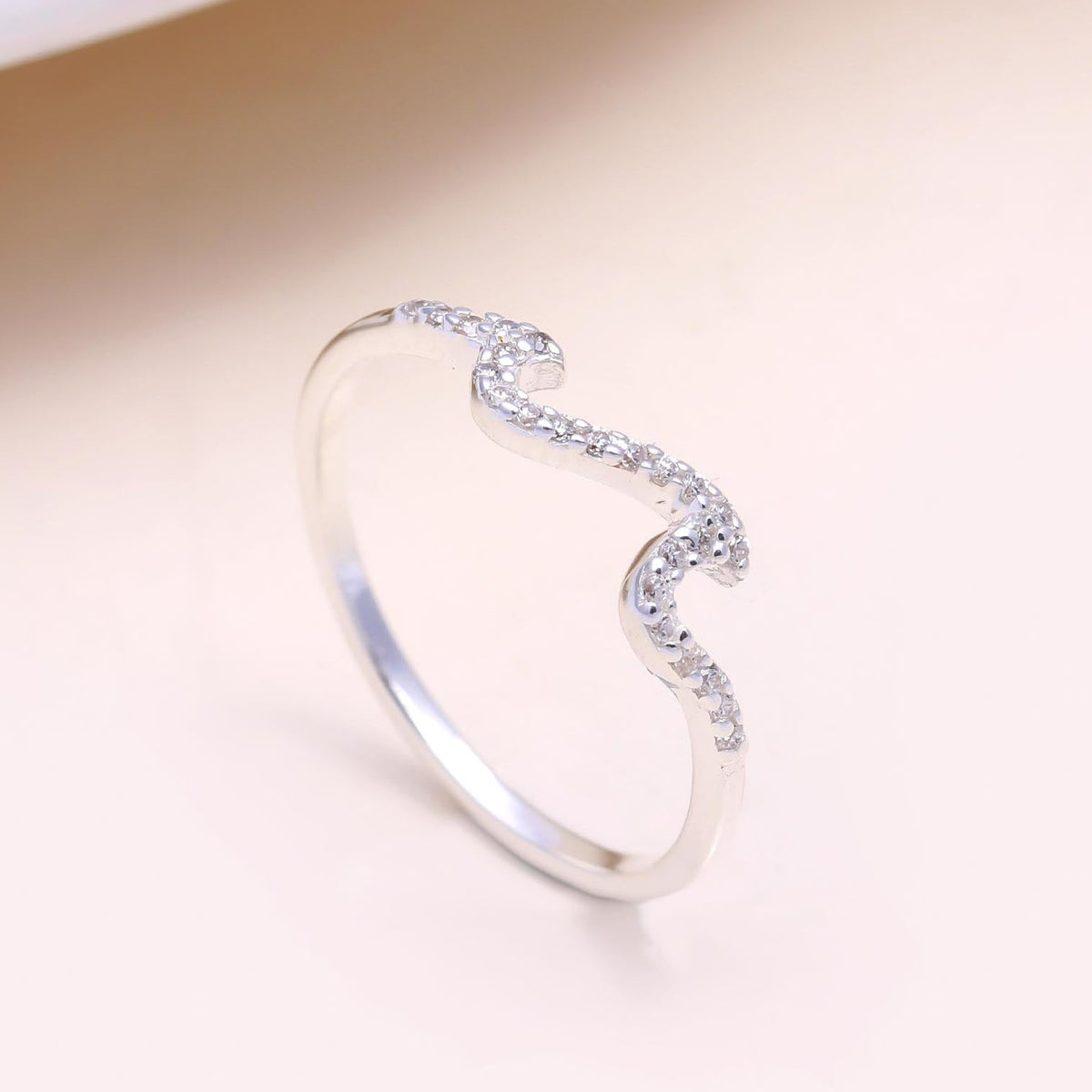 Silver ring with a wavy design on a beige background