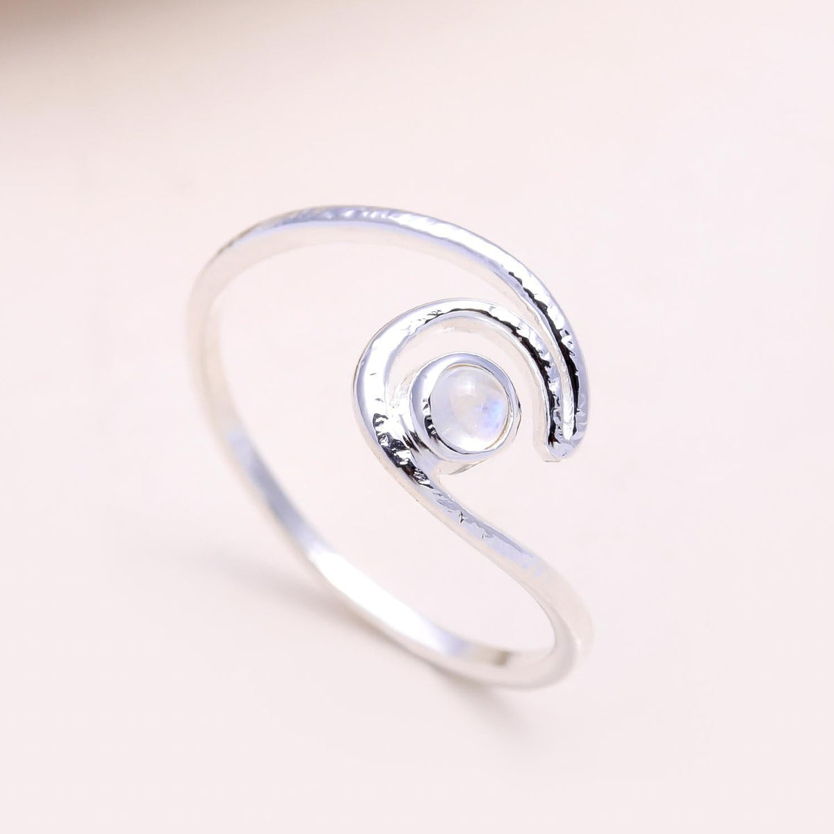 Silver ring with a central gemstone on a light pink background