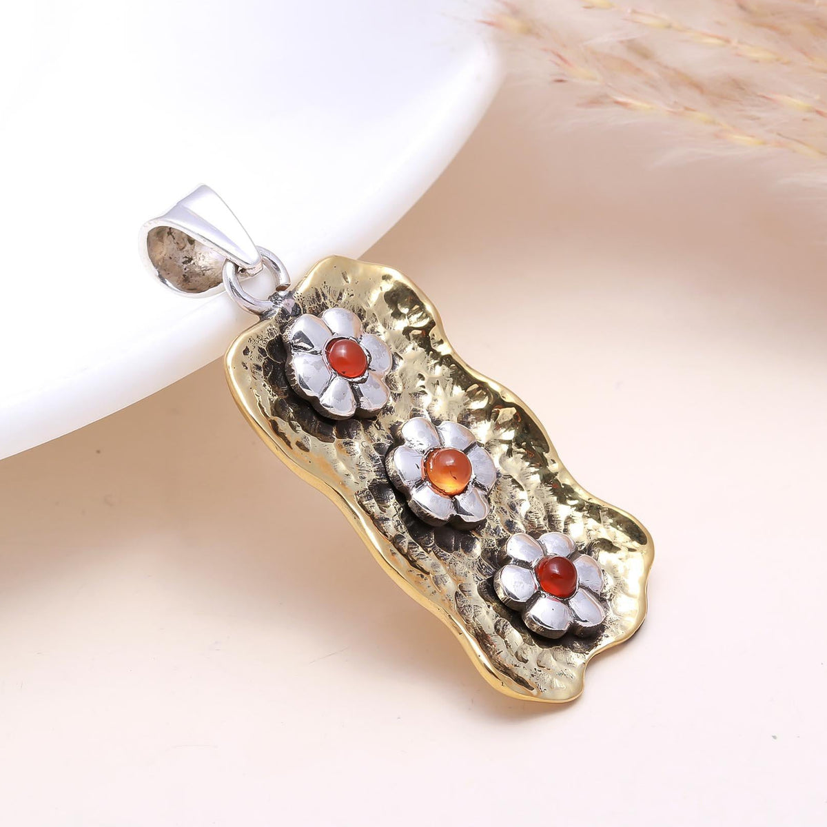 Gold and silver pendant with floral designs on a beige surface