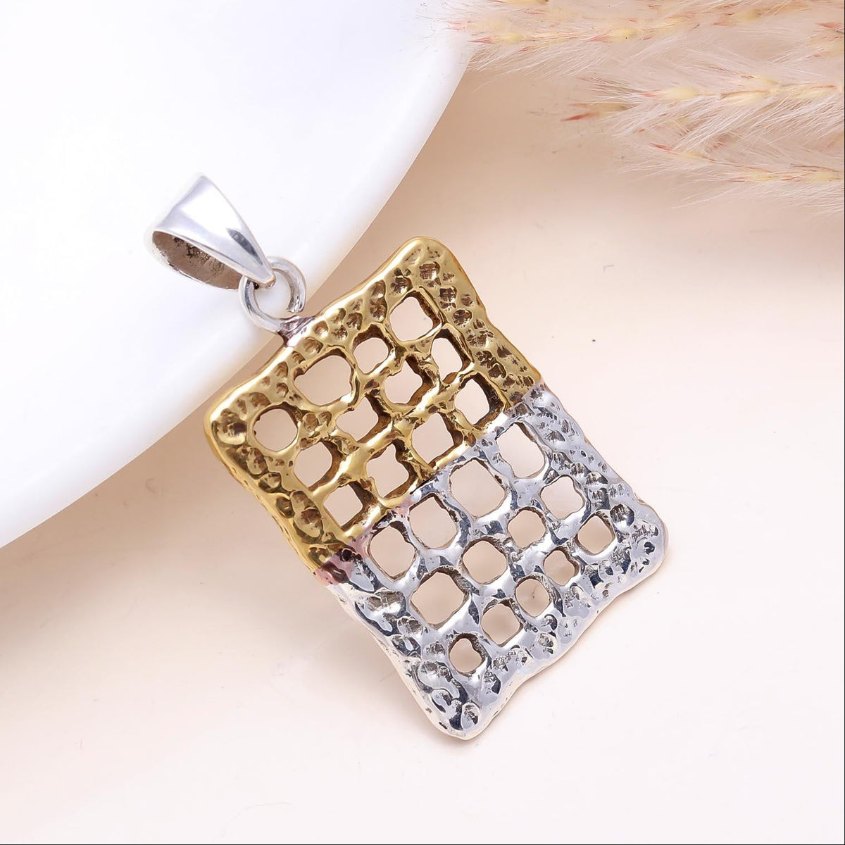 Two-tone gold and silver pendant on a white surface with a textured beige background