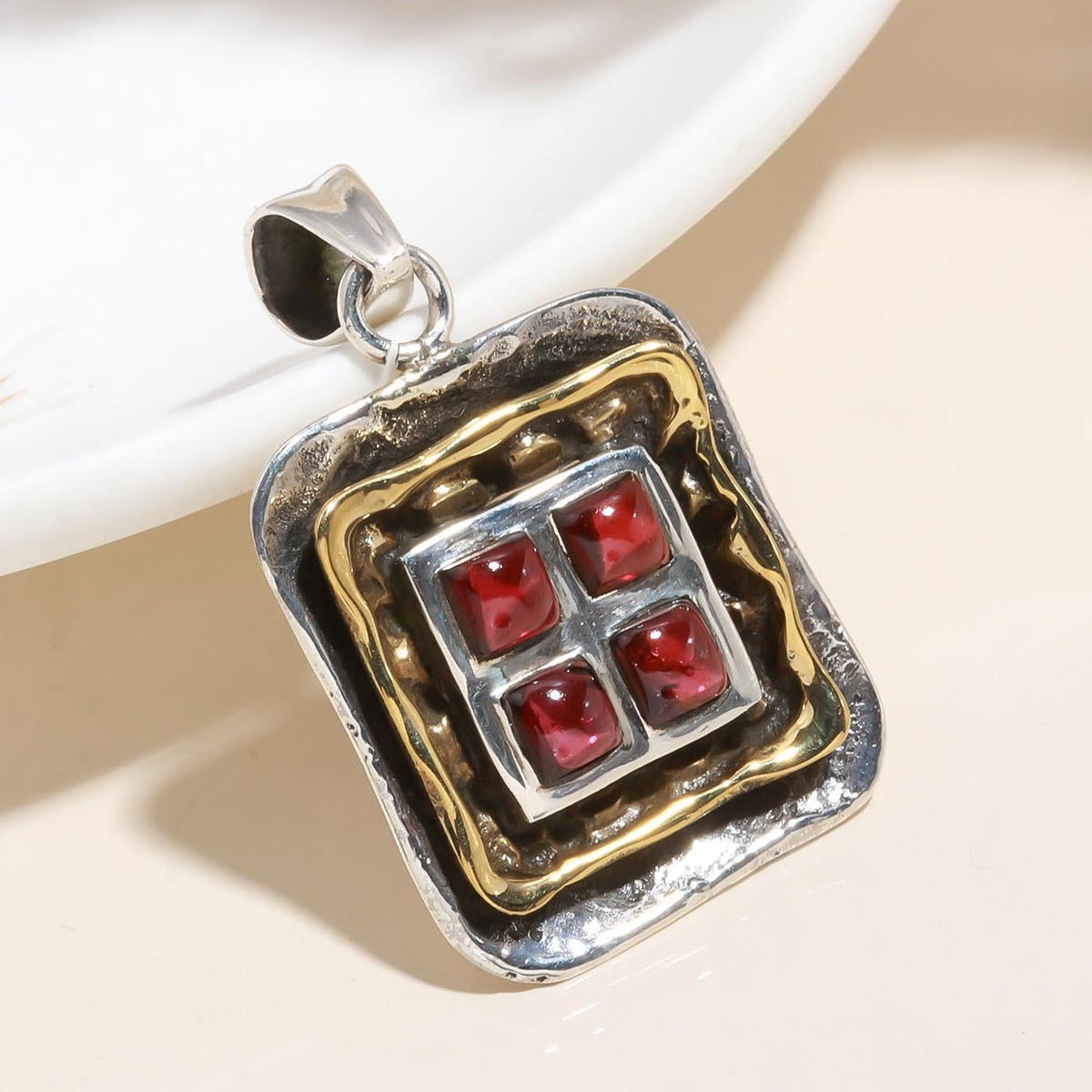 Silver and gold pendant with red stones on a beige surface