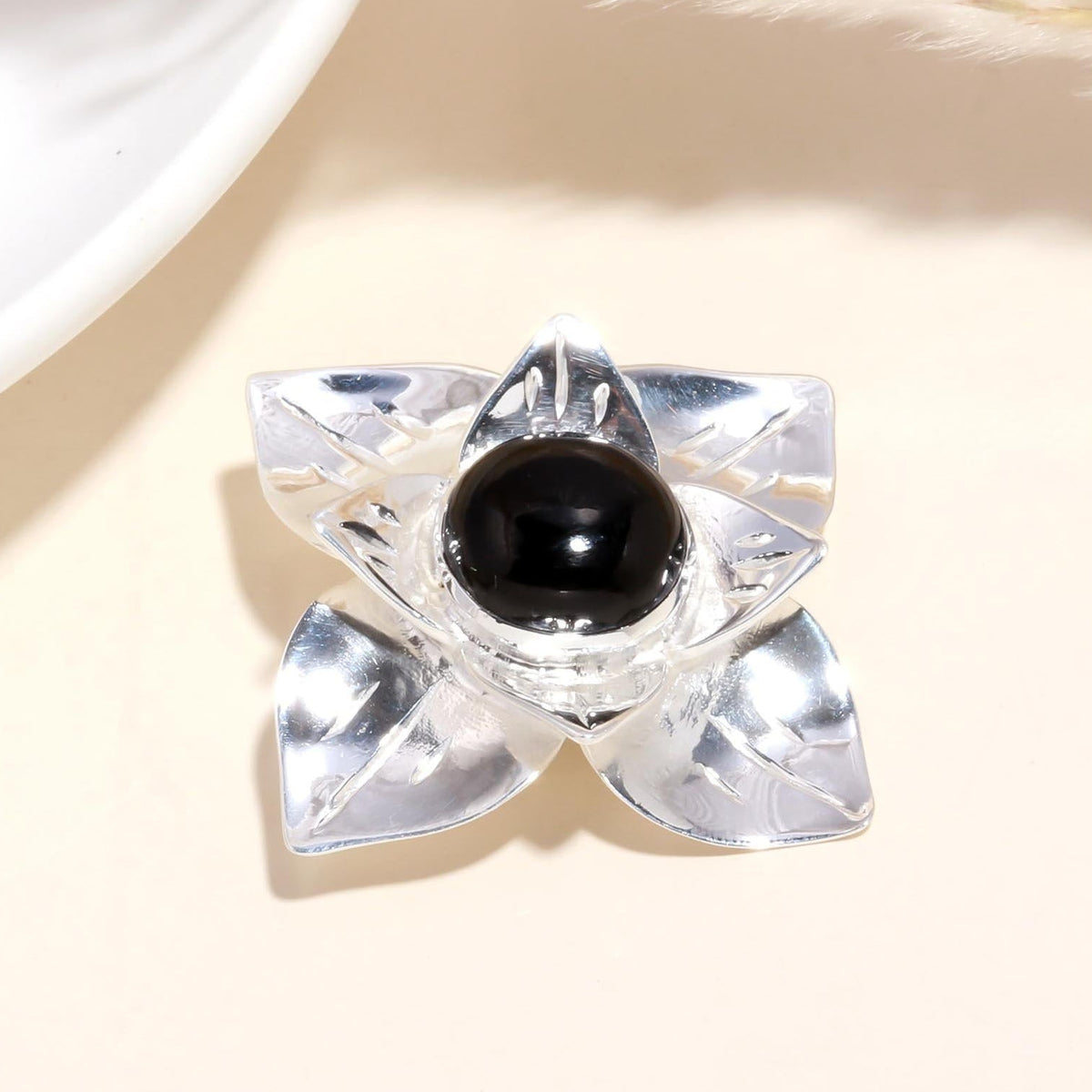 A 925 sterling silver ring with a floral-inspired design featuring a bold black onyx gemstone at the center, displayed on a beige background.