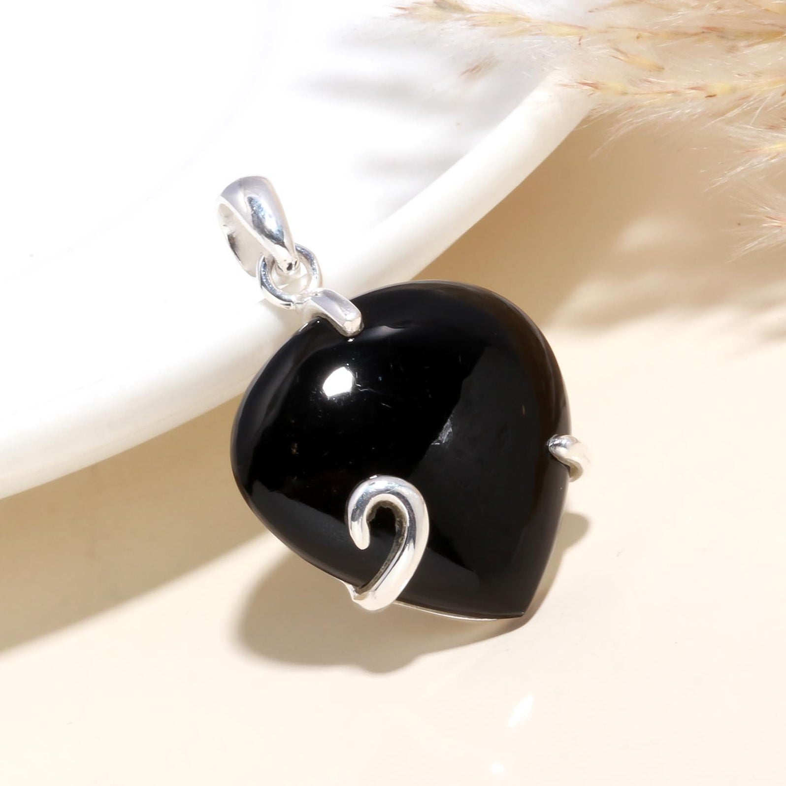 A heart-shaped black onyx gemstone pendant with a polished silver setting, displayed against a light background.