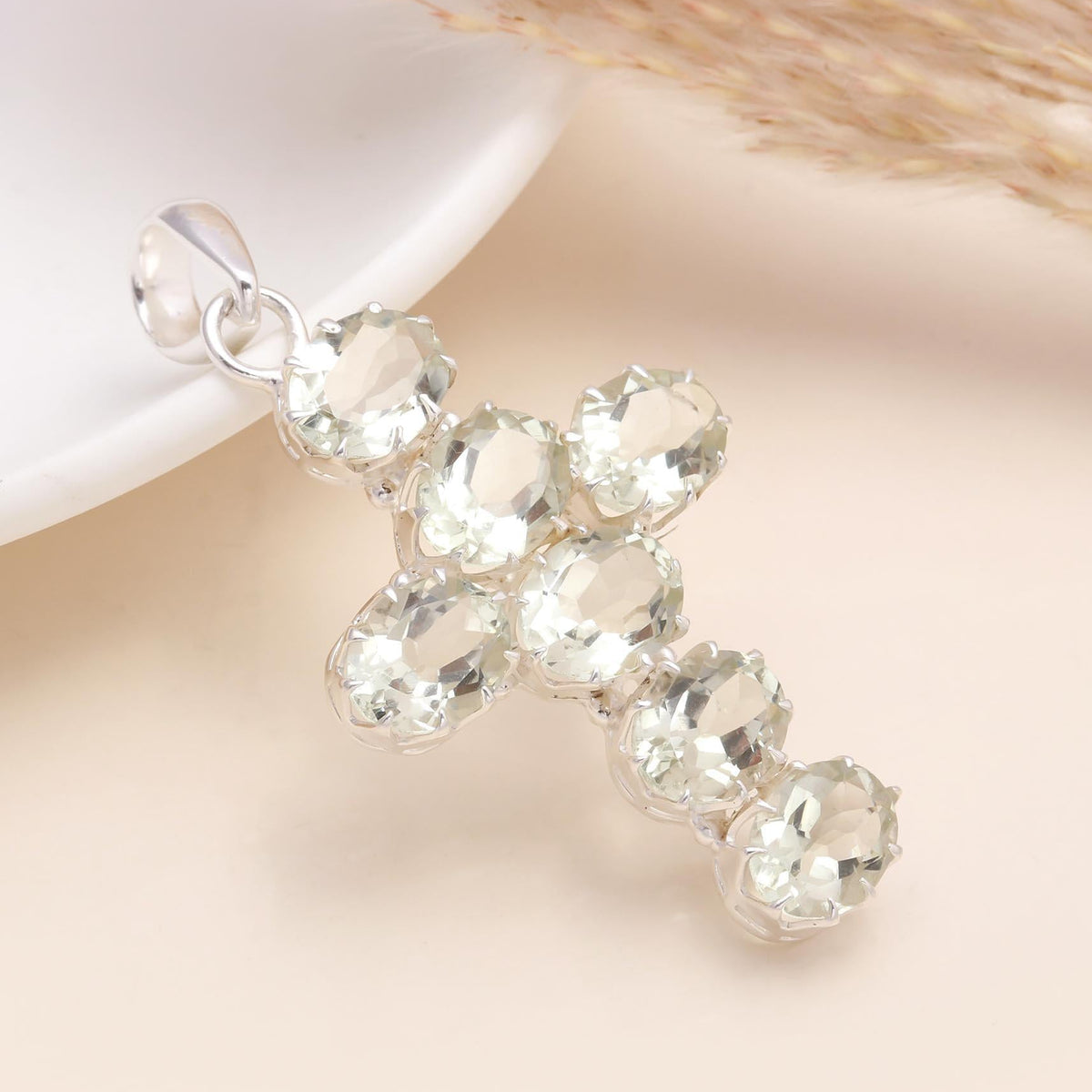 Silver cross pendant with clear gemstones on a soft beige background