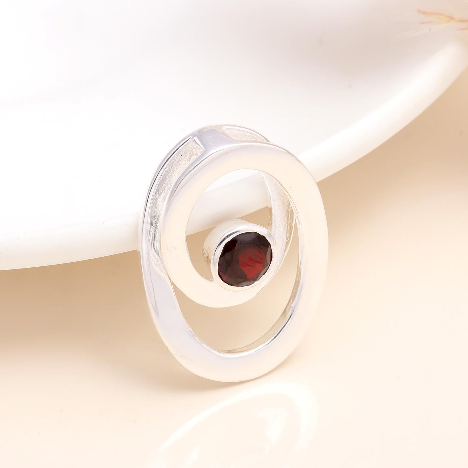 A 925 sterling silver modern garnet spiral pendant on a white surface, featuring a natural deep-red garnet gemstone.
