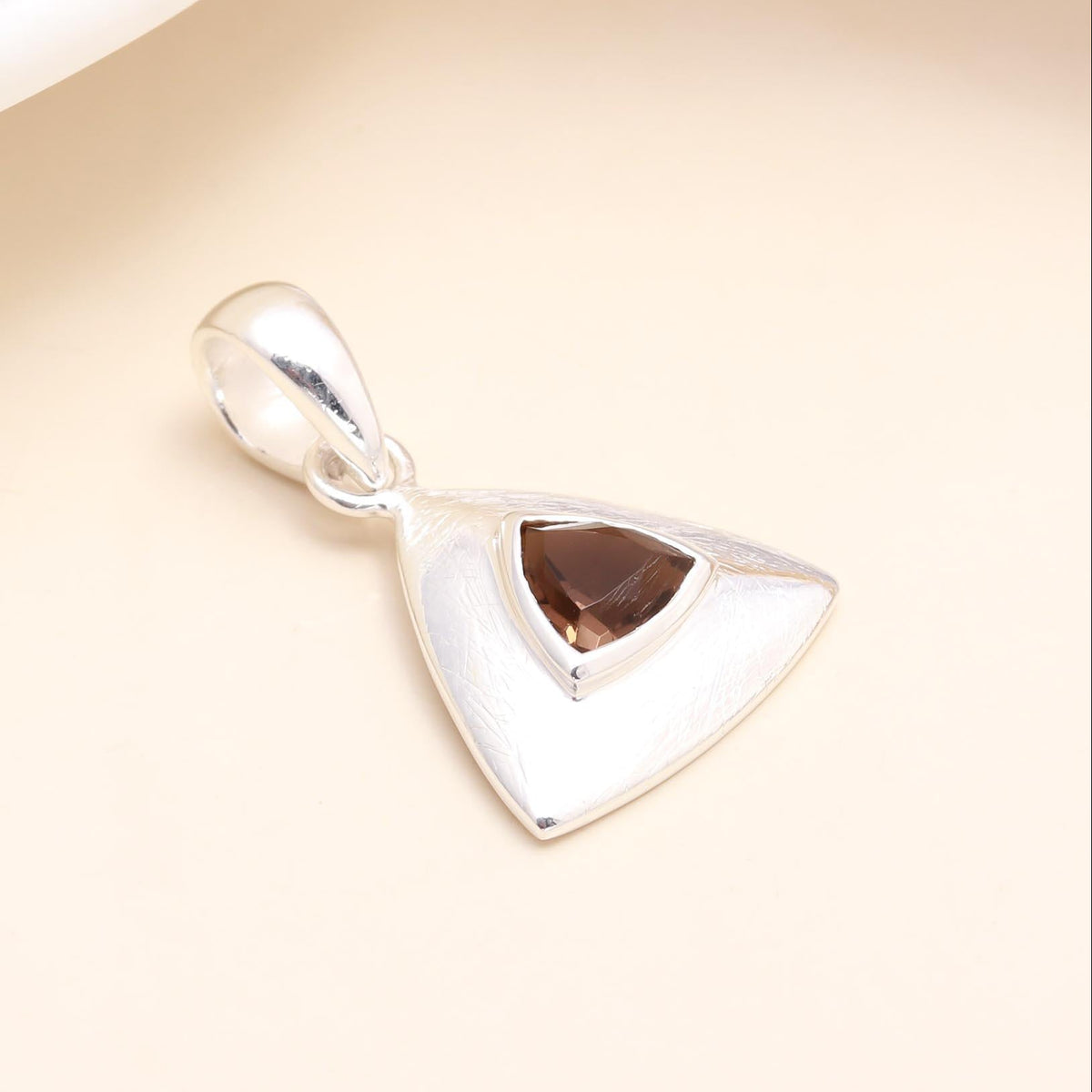 Silver pendant with a triangular gemstone on a beige background