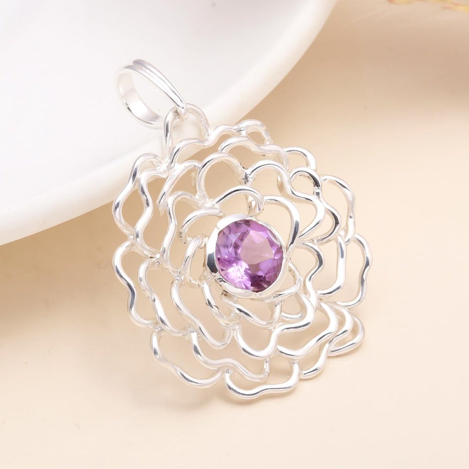 Silver floral pendant with a purple gemstone on a soft beige background
