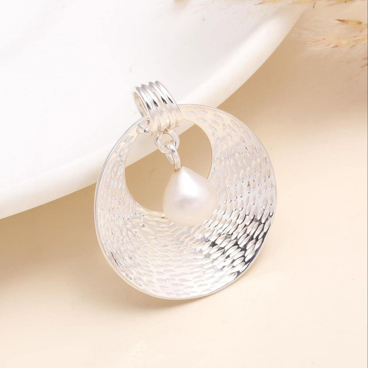 Silver pendant with a pearl on a beige background