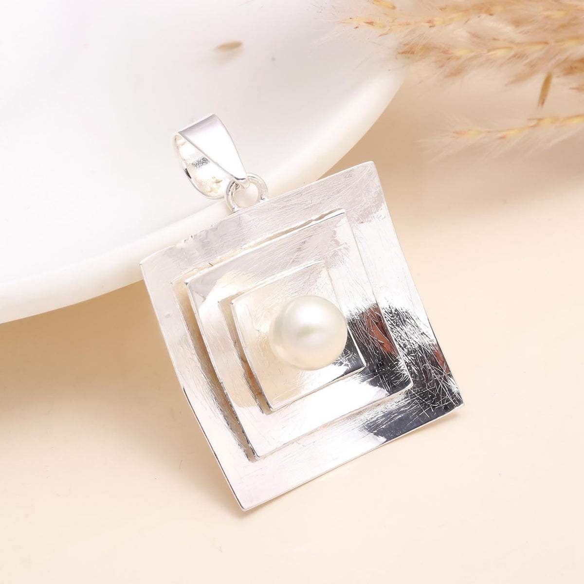 Silver pendant with a pearl on a beige background