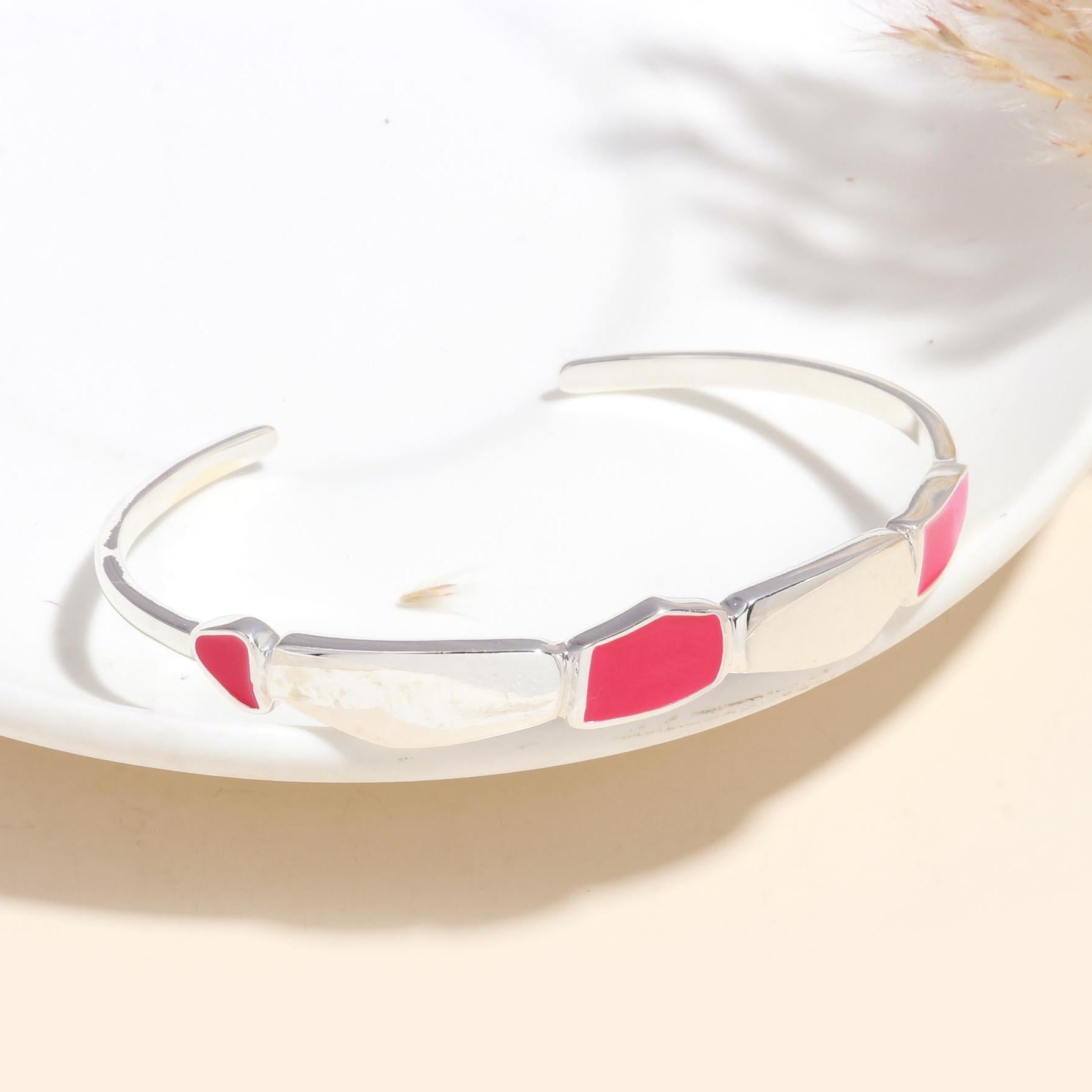 A 925 sterling silver cuff bracelet with pink enamel detailing, displayed on a white plate.