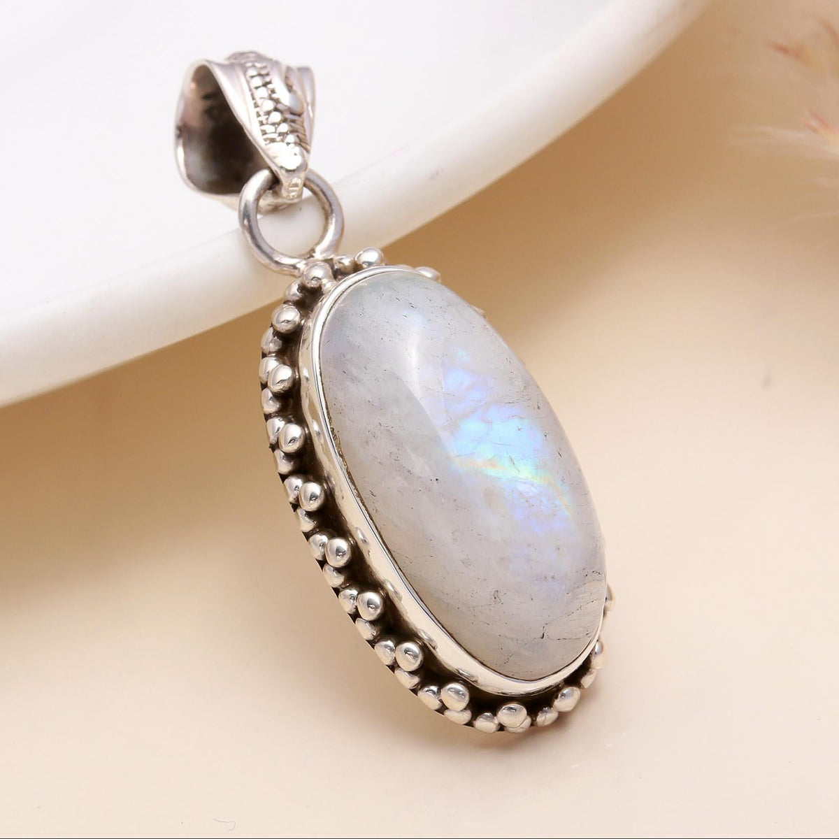 A 925 Sterling Silver pendant featuring an oval Rainbow Moonstone with a classic setting, displayed against a neutral background.