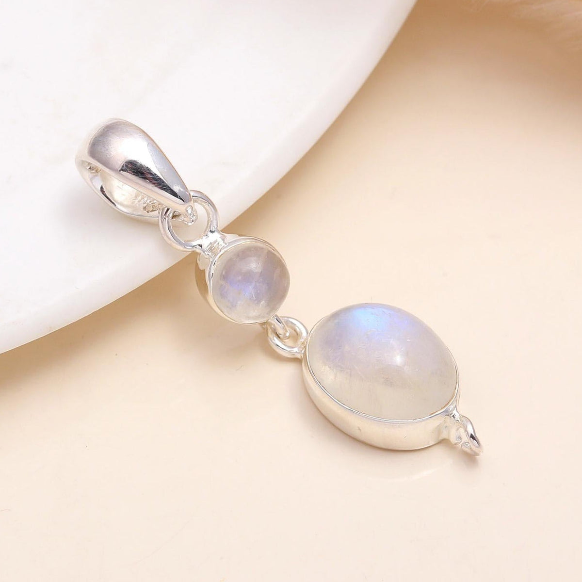 A silver pendant featuring two round rainbow moonstones set in a double moonstone design, presented on a white dish.