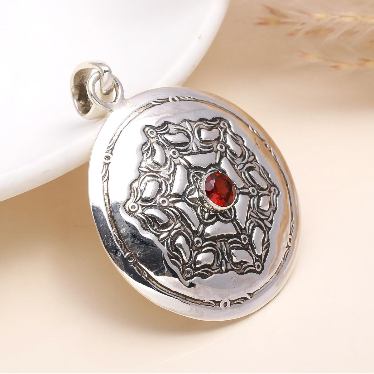 A vintage round medallion garnet pendant made of 925 sterling silver with intricate silver detailing and a red garnet centerpiece.