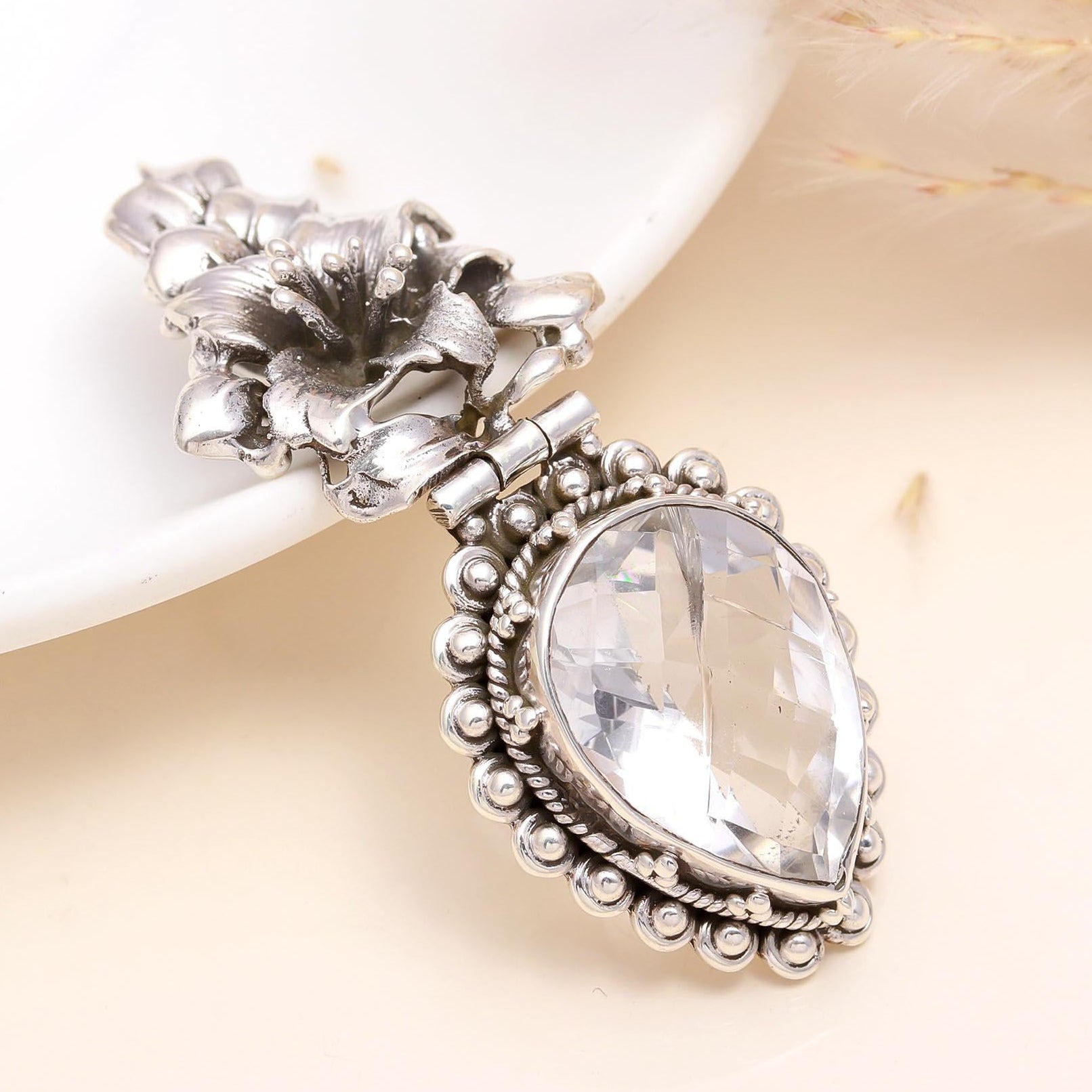 A sterling silver vintage floral design teardrop crystal pendant with intricate details and a shiny finish.