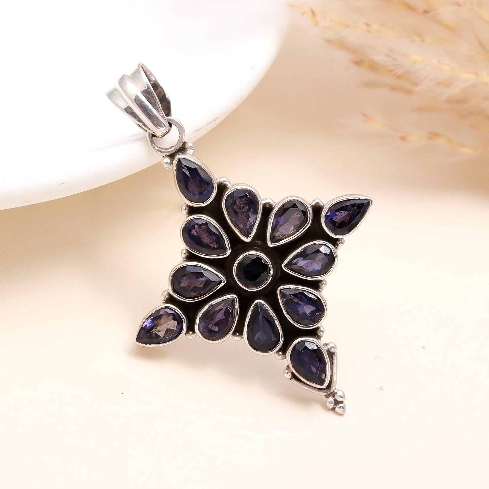 A sterling silver pendant with a natural blue iolite gemstone, featuring a floral design with multiple petals around the gemstone.