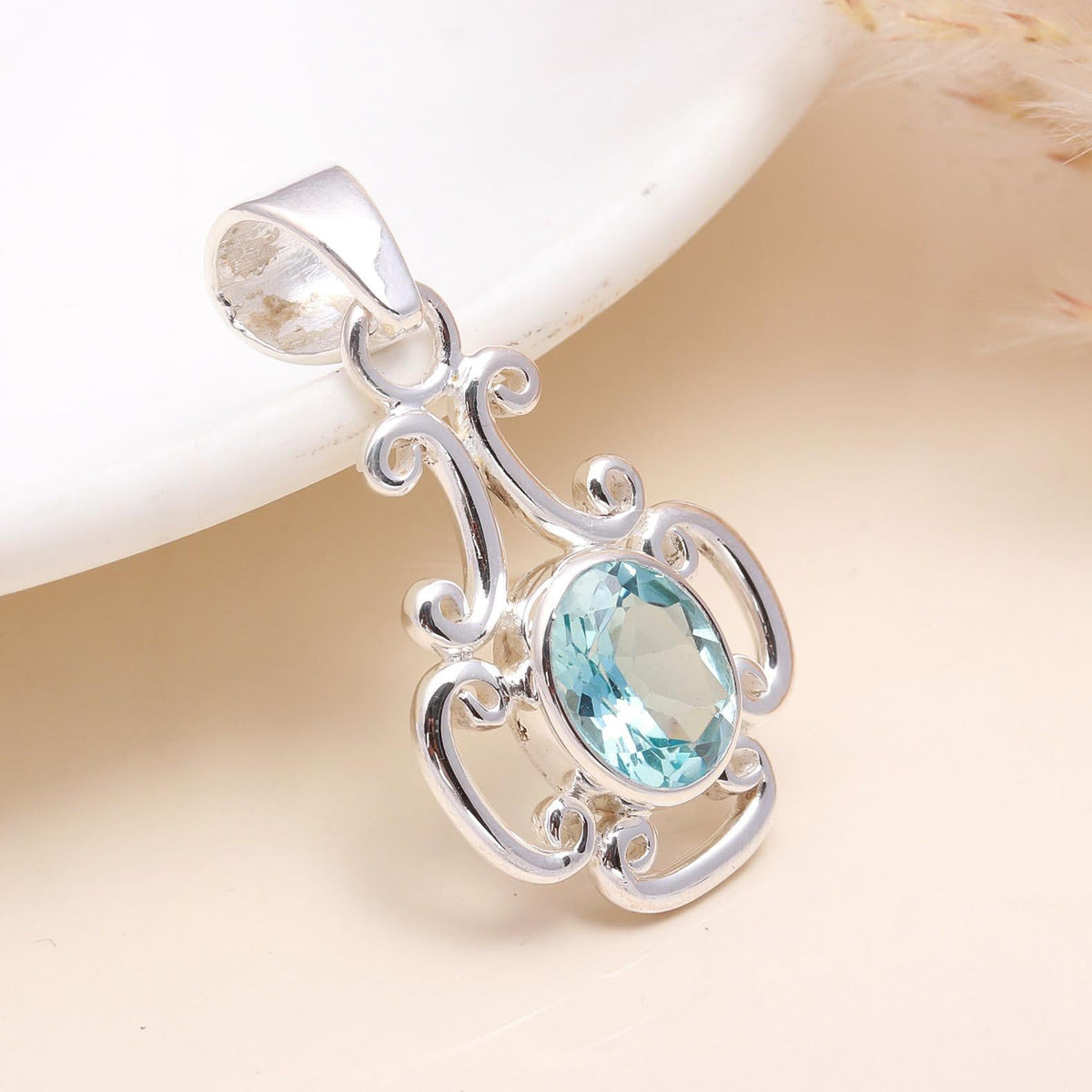 A sterling silver pendant with a blue topaz gemstone, featuring an elegant intricate mounting design.