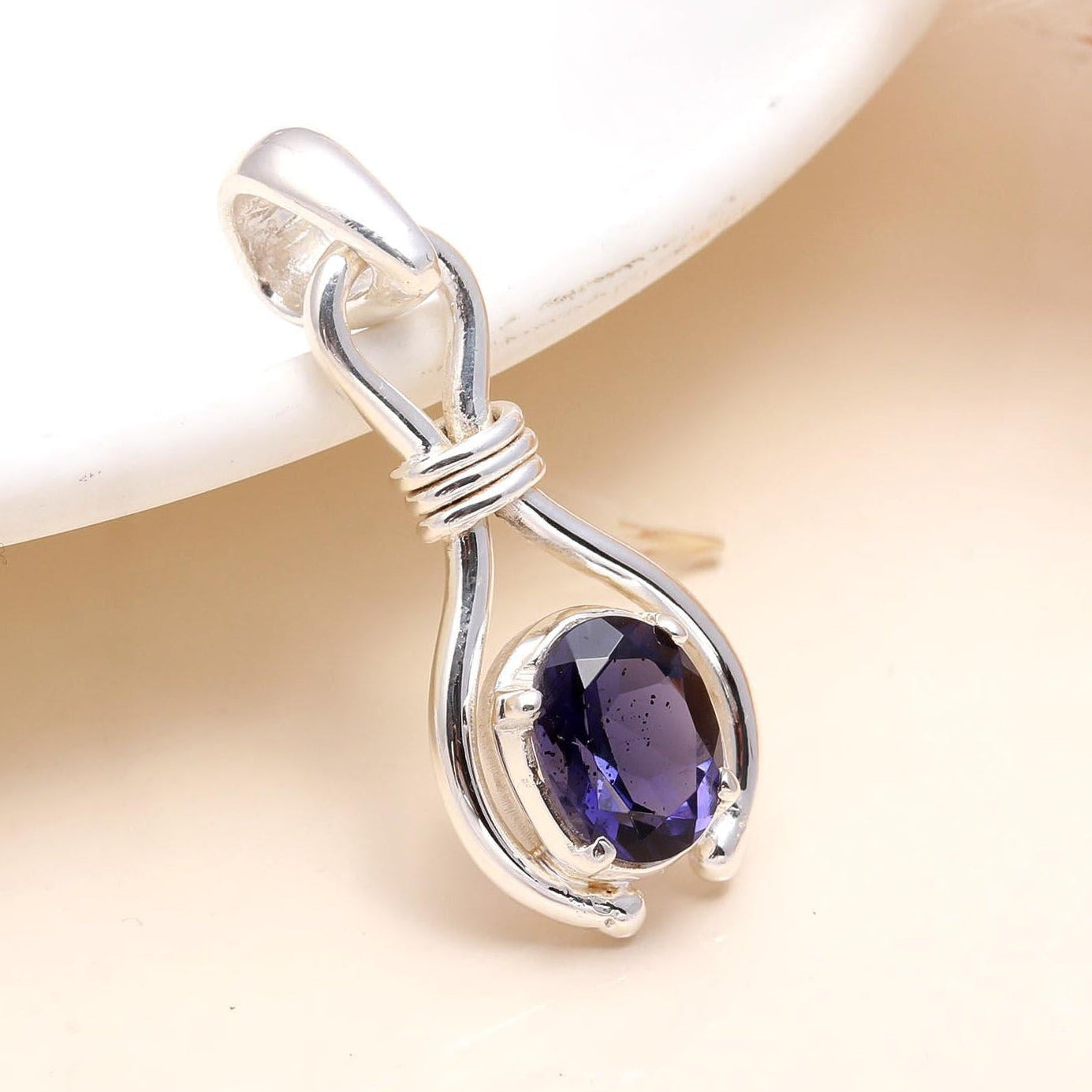 A 925 Sterling Silver Blue Faceted Iolite Pendant placed on a white surface, highlighting the gemstone's facades and the silver mounting.