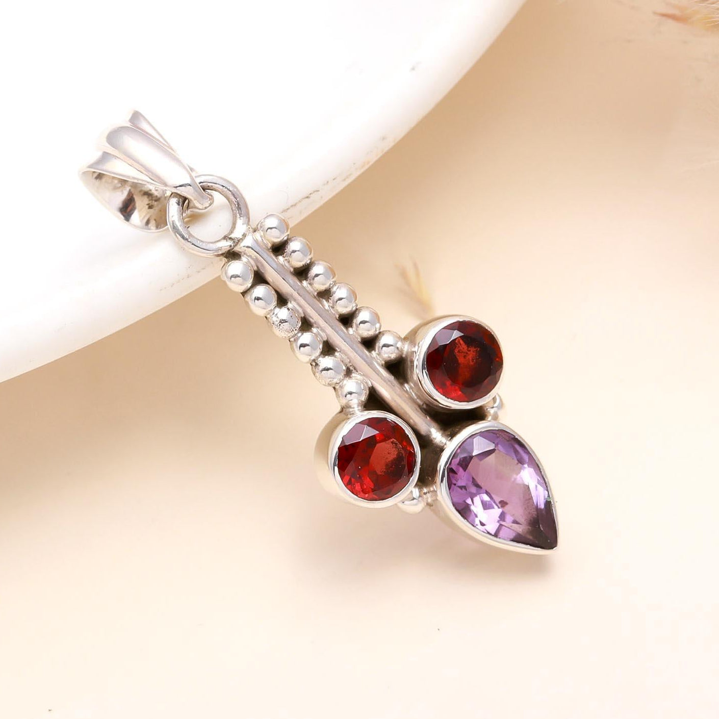 A sterling silver pendant featuring a combination of deep purple amethyst and rich red garnet gemstones, set in a vintage-style filigree silver frame.