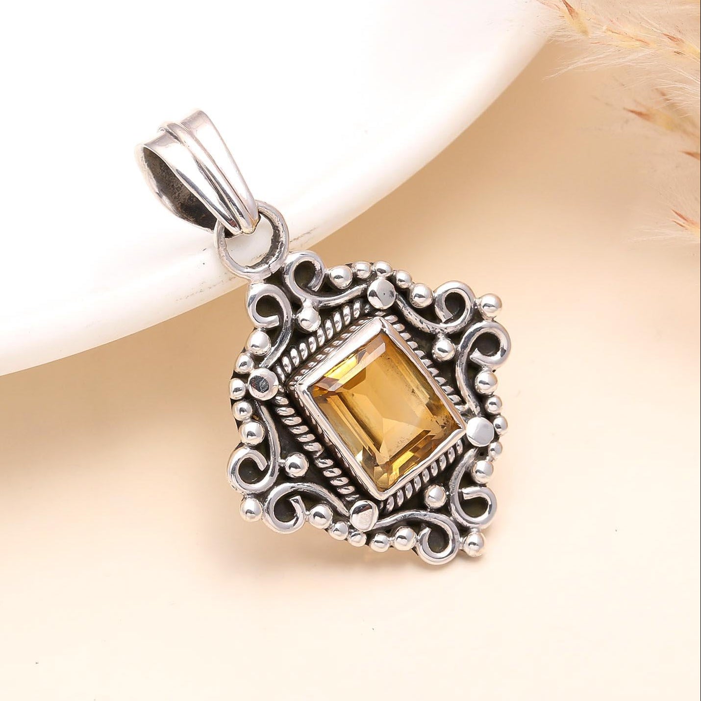 A vintage-inspired boho pendant made of sterling silver with a natural citrine gemstone, presented against a neutral background.