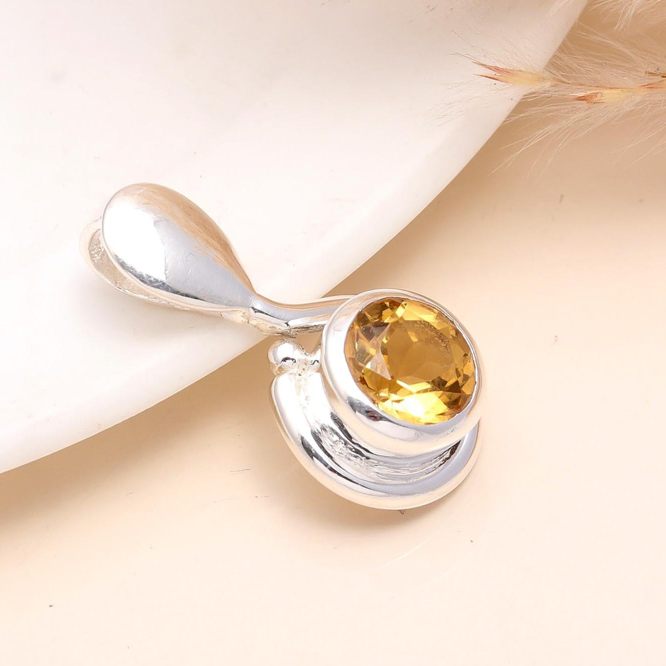 A sterling silver pendant with a teardrop-shaped citrine gemstone, presented on a white surface with soft lighting.