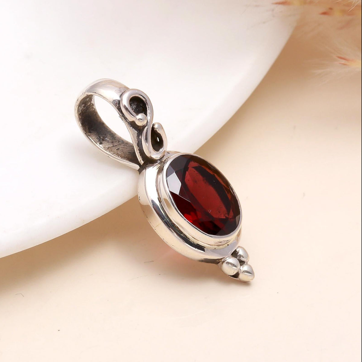 A sterling silver pendant with an oval-cut garnet, presented on a white surface.