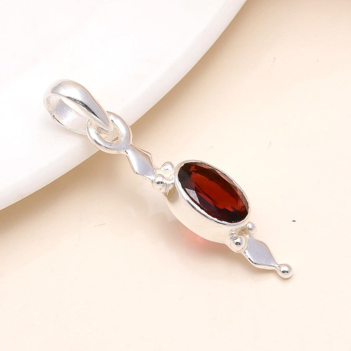 Silver pendant with a red gemstone on a beige background