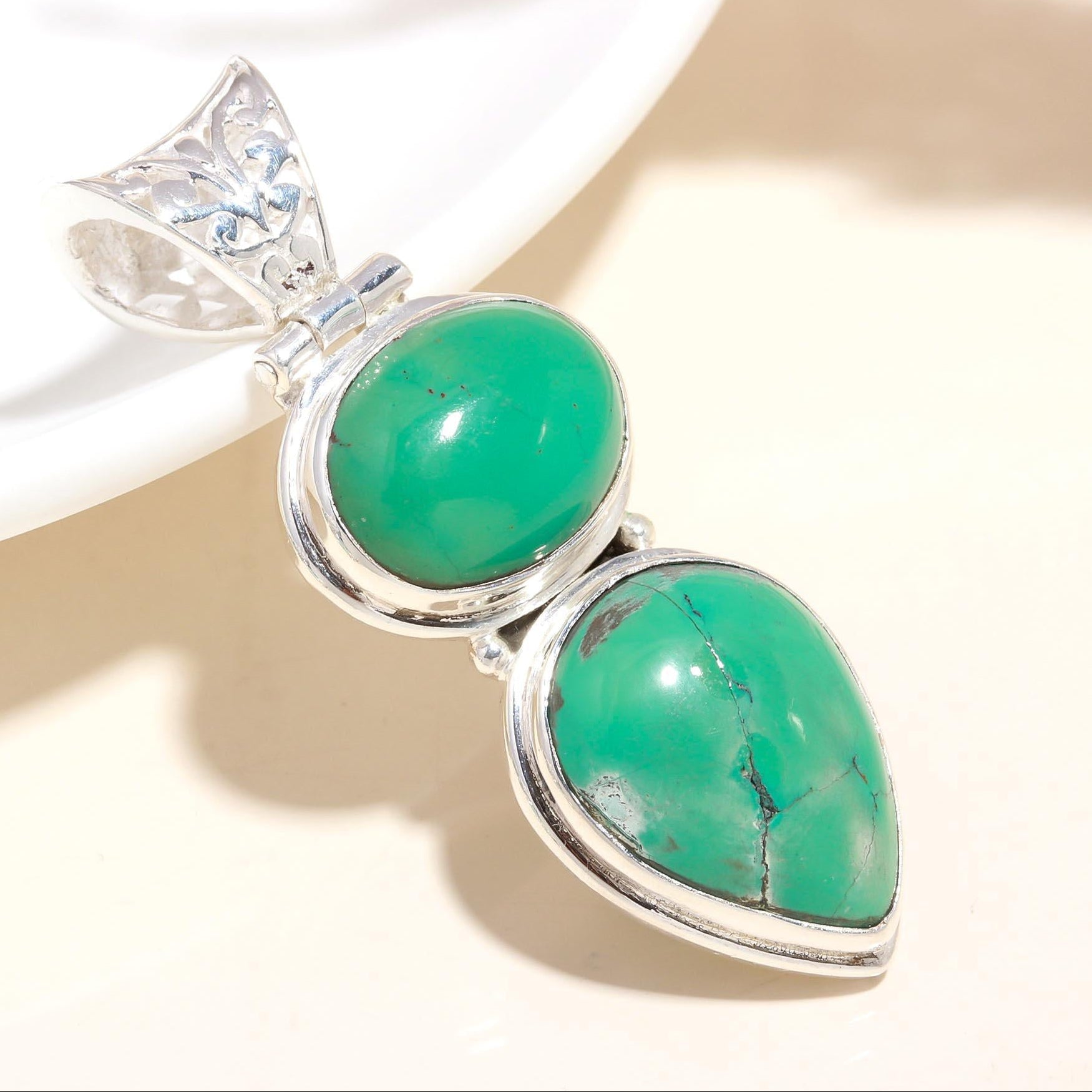 A sterling silver pendant with a double stone green turquoise design, featuring intricate silver detailing and a unique artisanal finish.
