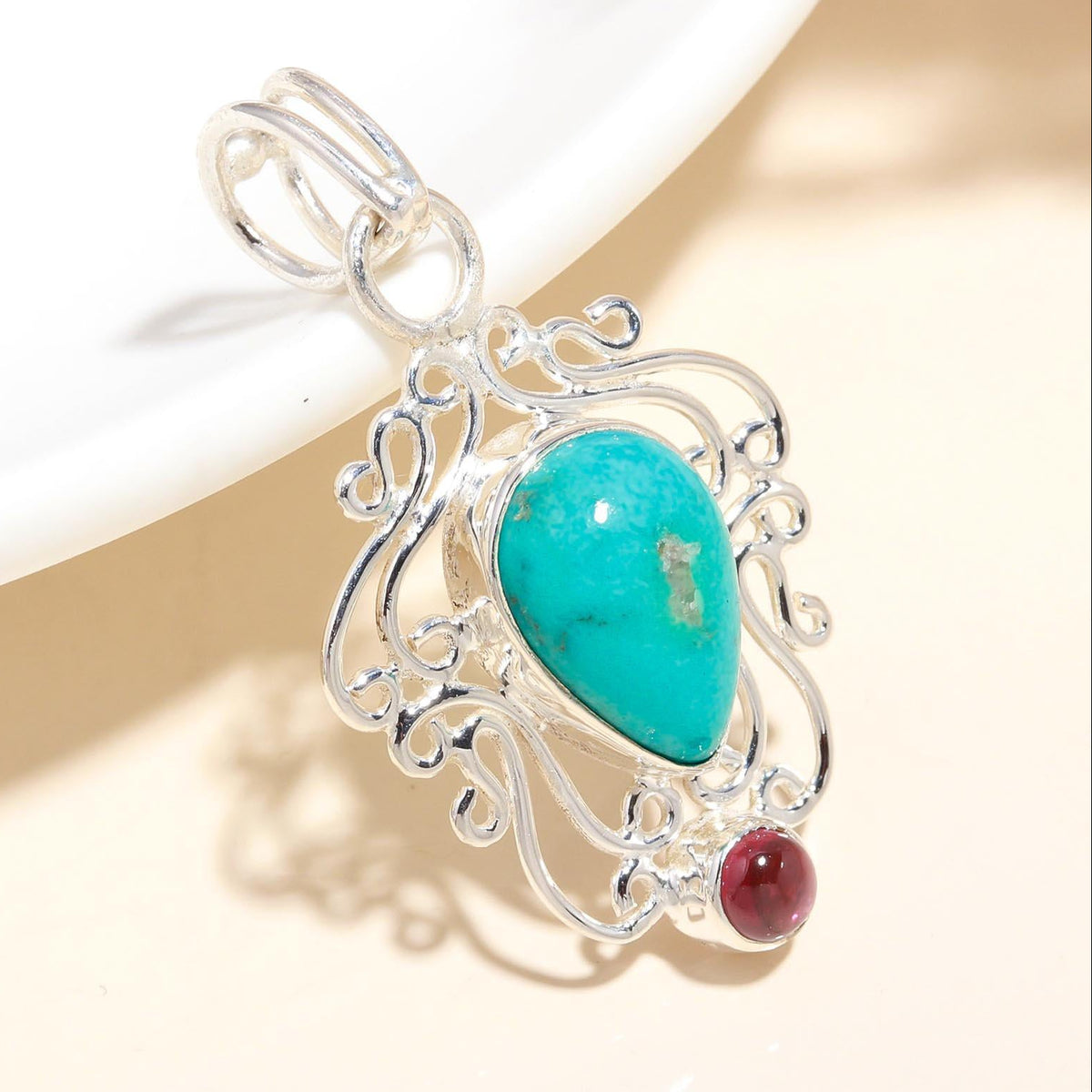 A sterling silver pendant featuring a turquoise stone and a garnet stone, with intricate filigree detailing.