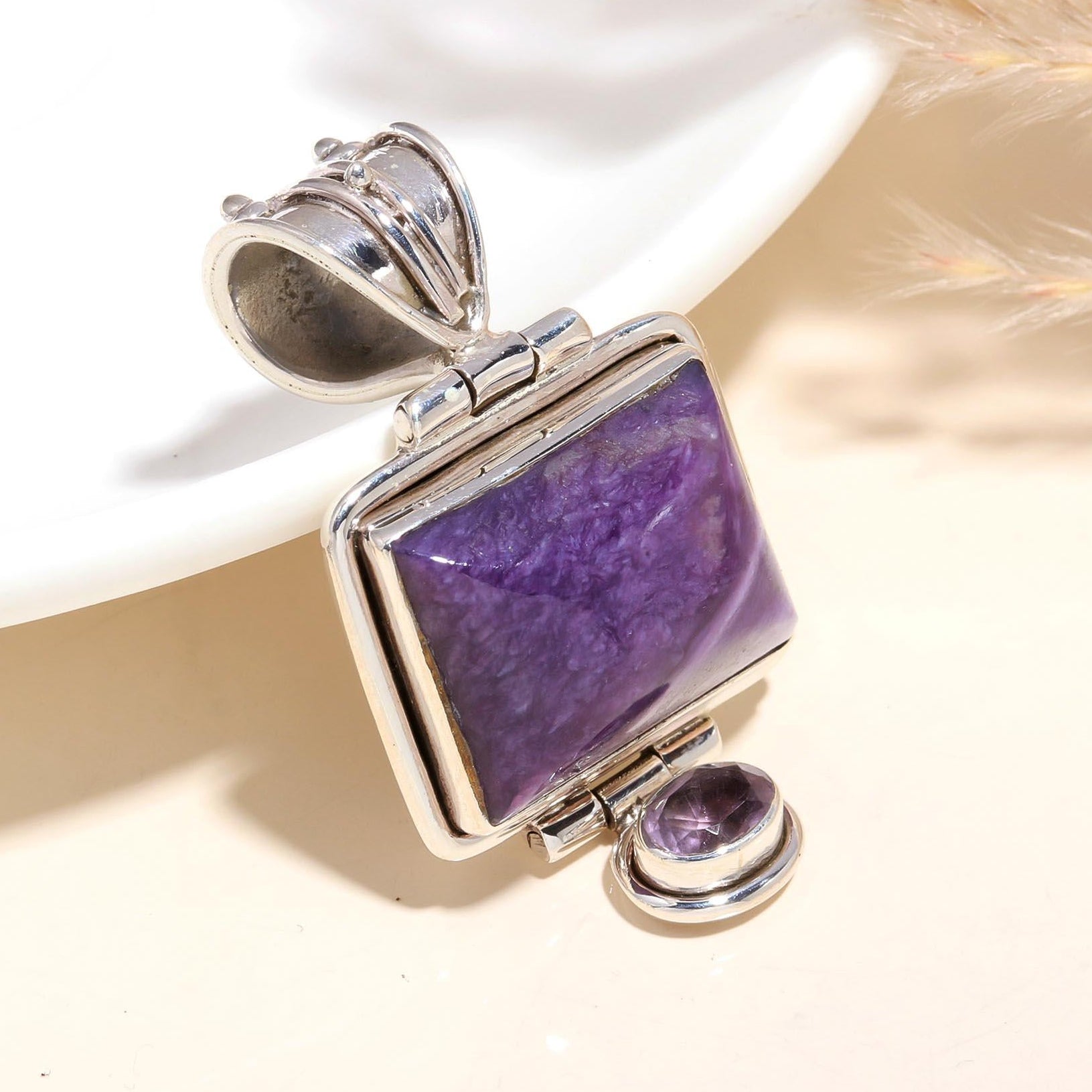 A sterling silver vintage-style locket pendant featuring a purple charoite gemstone, displayed against a neutral background.