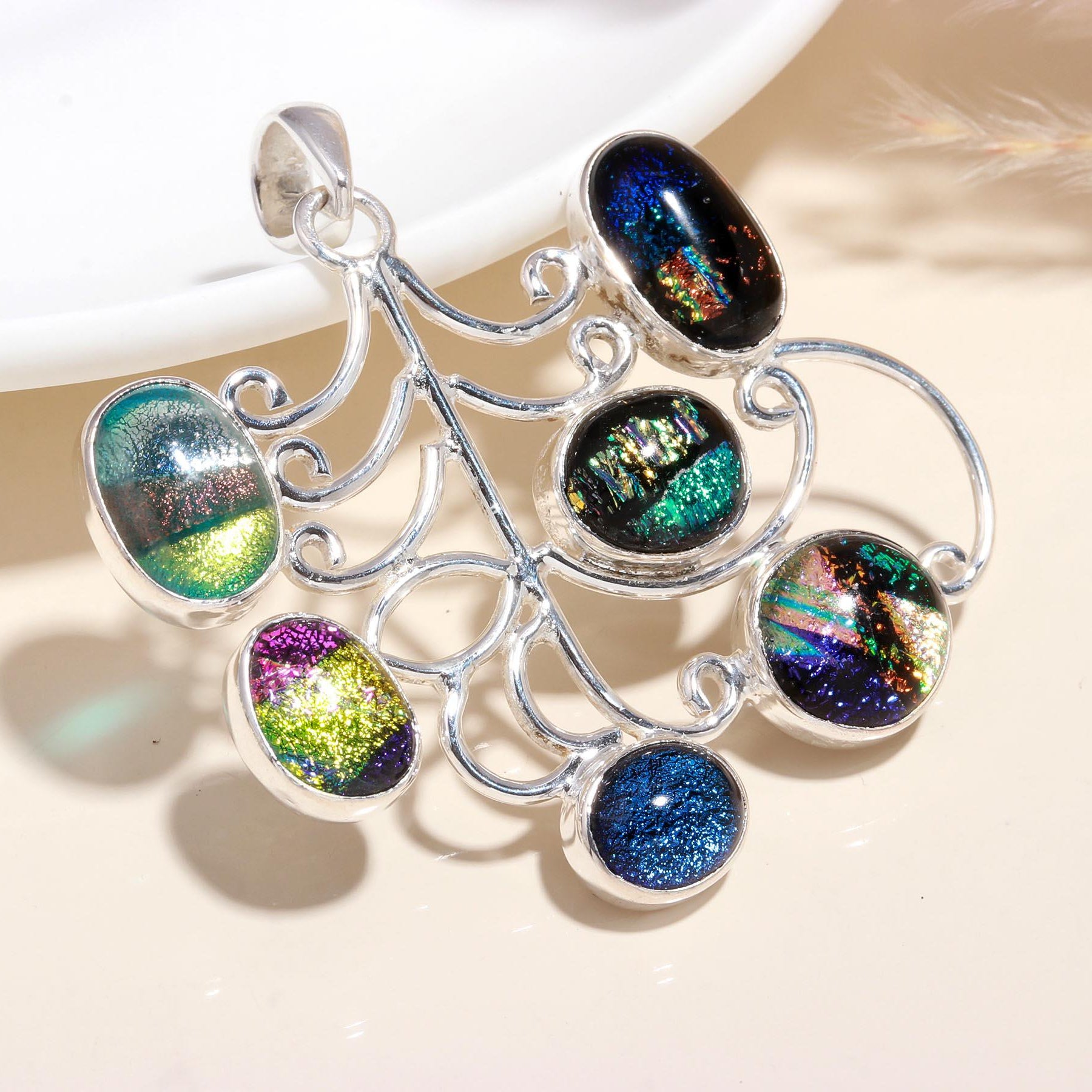 A sterling silver pendant with a geometric pattern and multipleicolored dichroic glass inserts, displayed against a neutral background.