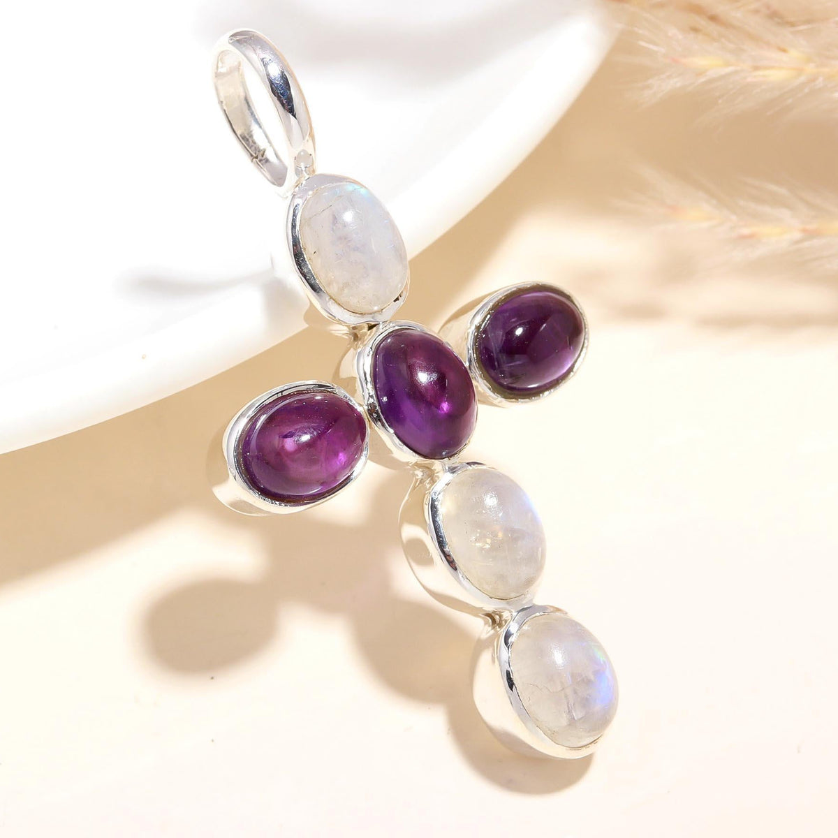 A sterling silver cross pendant featuring amethyst and moonstone gemstones, displayed against a neutral background.