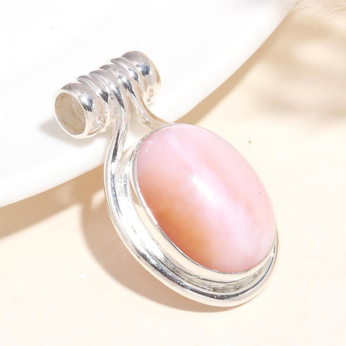 A pink conch shell pendant set in a silver mounting, displayed against a neutral background.