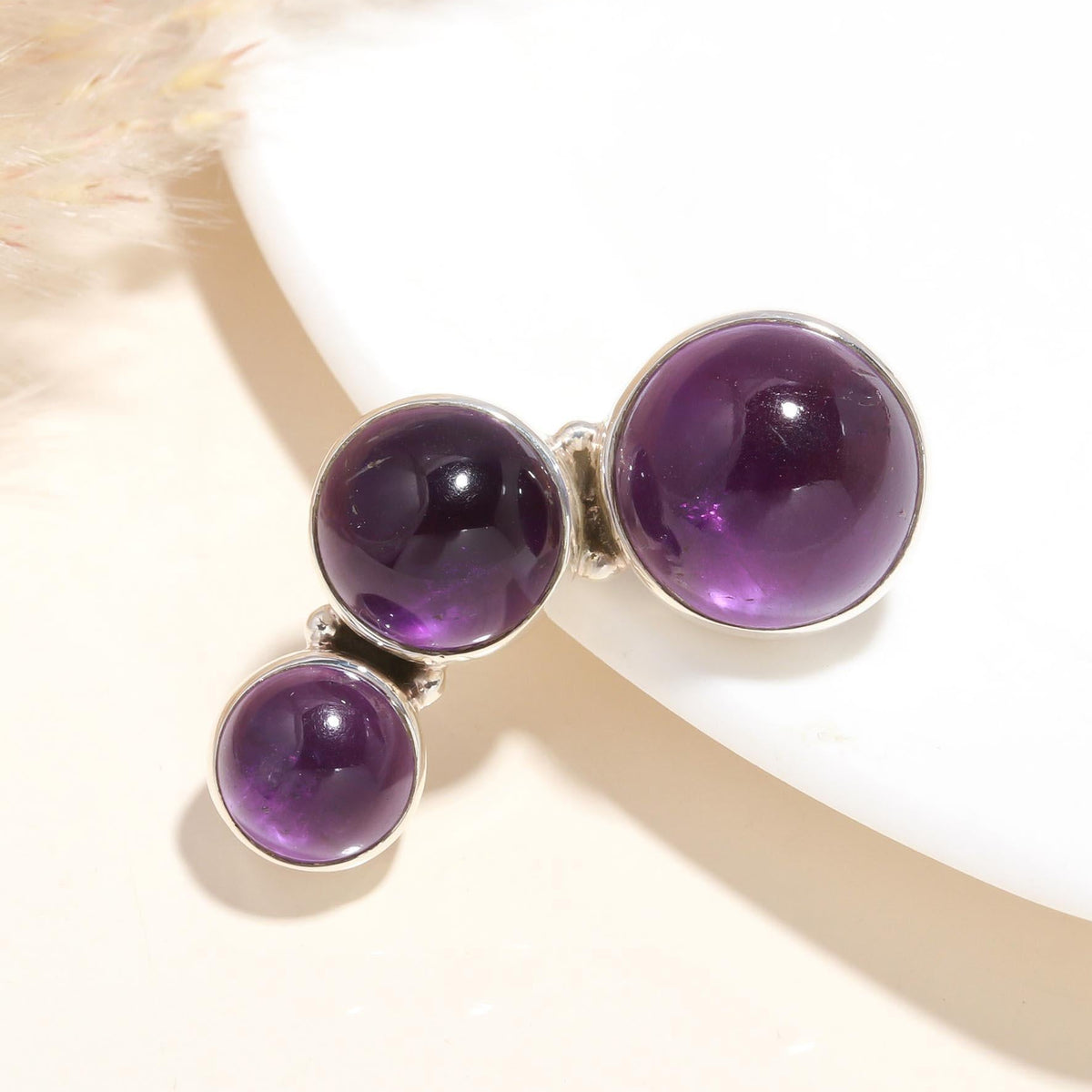 A sterling silver pendant with three natural amethyst gemstones, featuring intricate handcrafted silverwork.