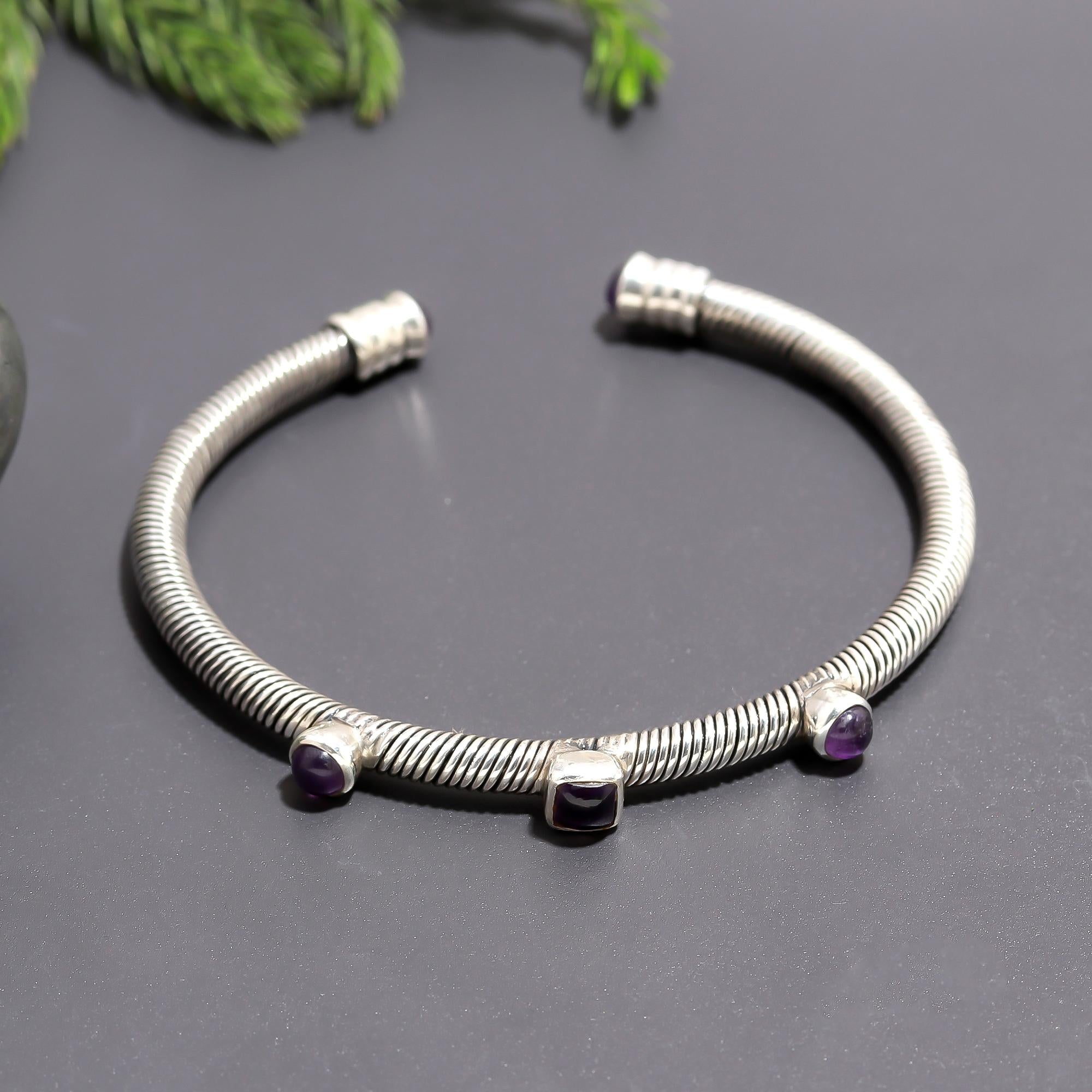 A 925 silver coil wire cuff bracelet with bezel-set amethyst and garnet stones on a grey background.