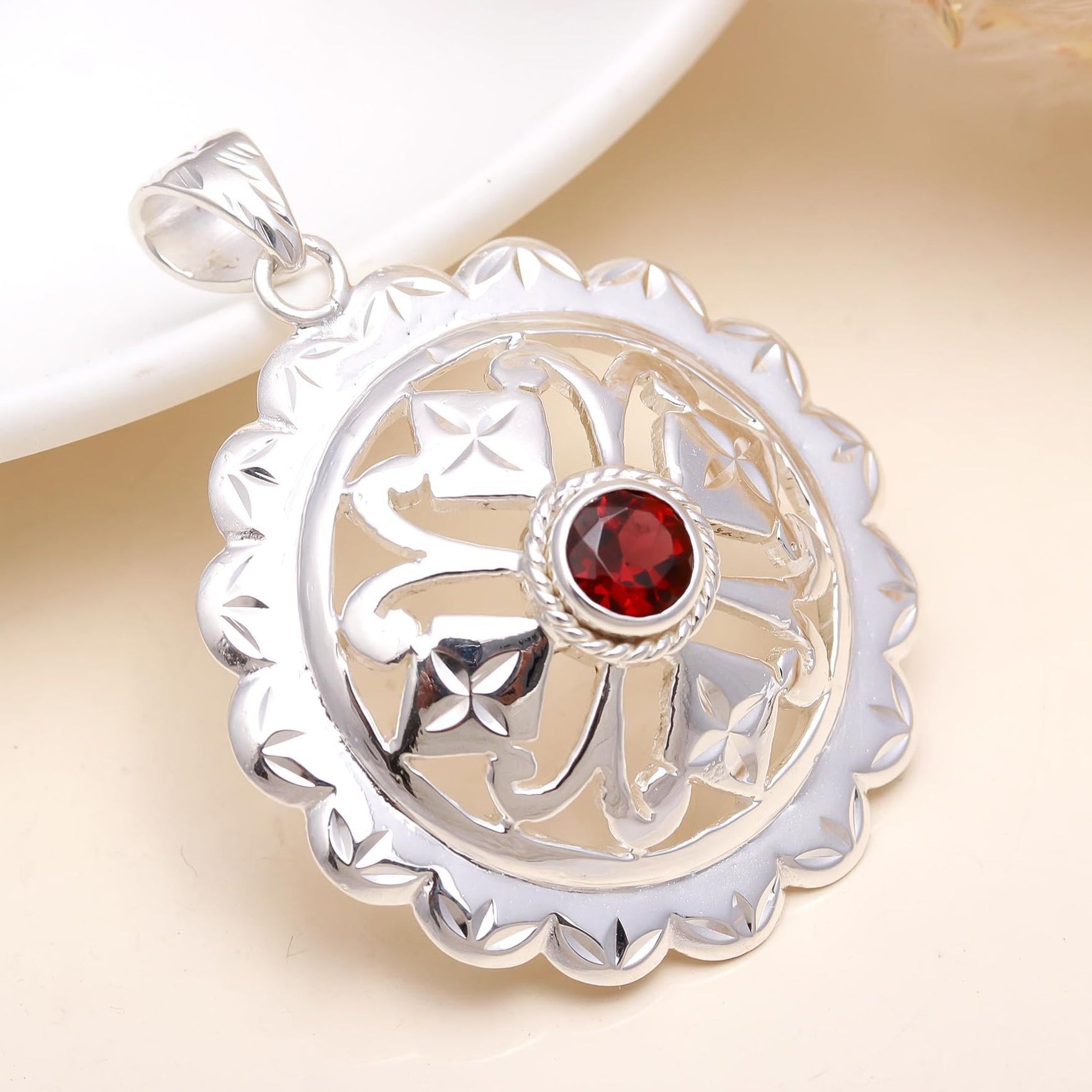 A sterling silver floral-patterned pendant with a red garnet gemstone in the center, displayed against a white background.