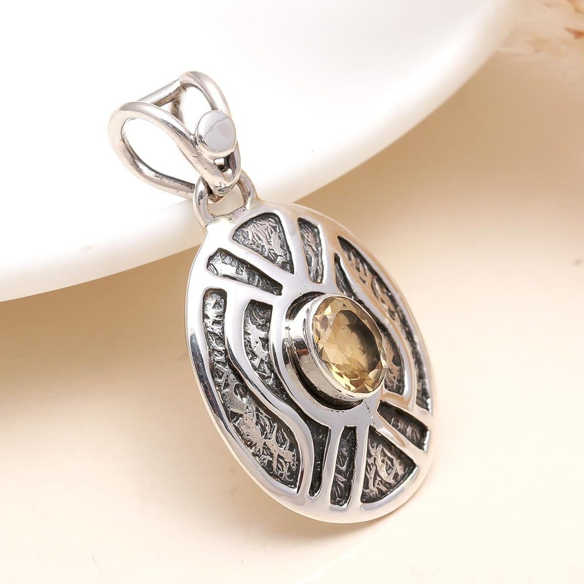 Silver pendant with a yellow gemstone on a soft beige background