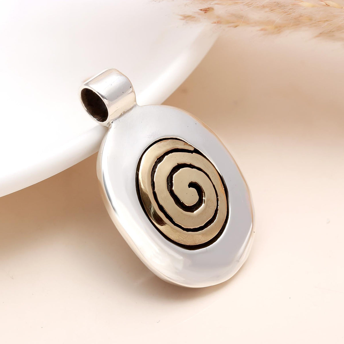 Silver pendant with a gold spiral design on a beige background