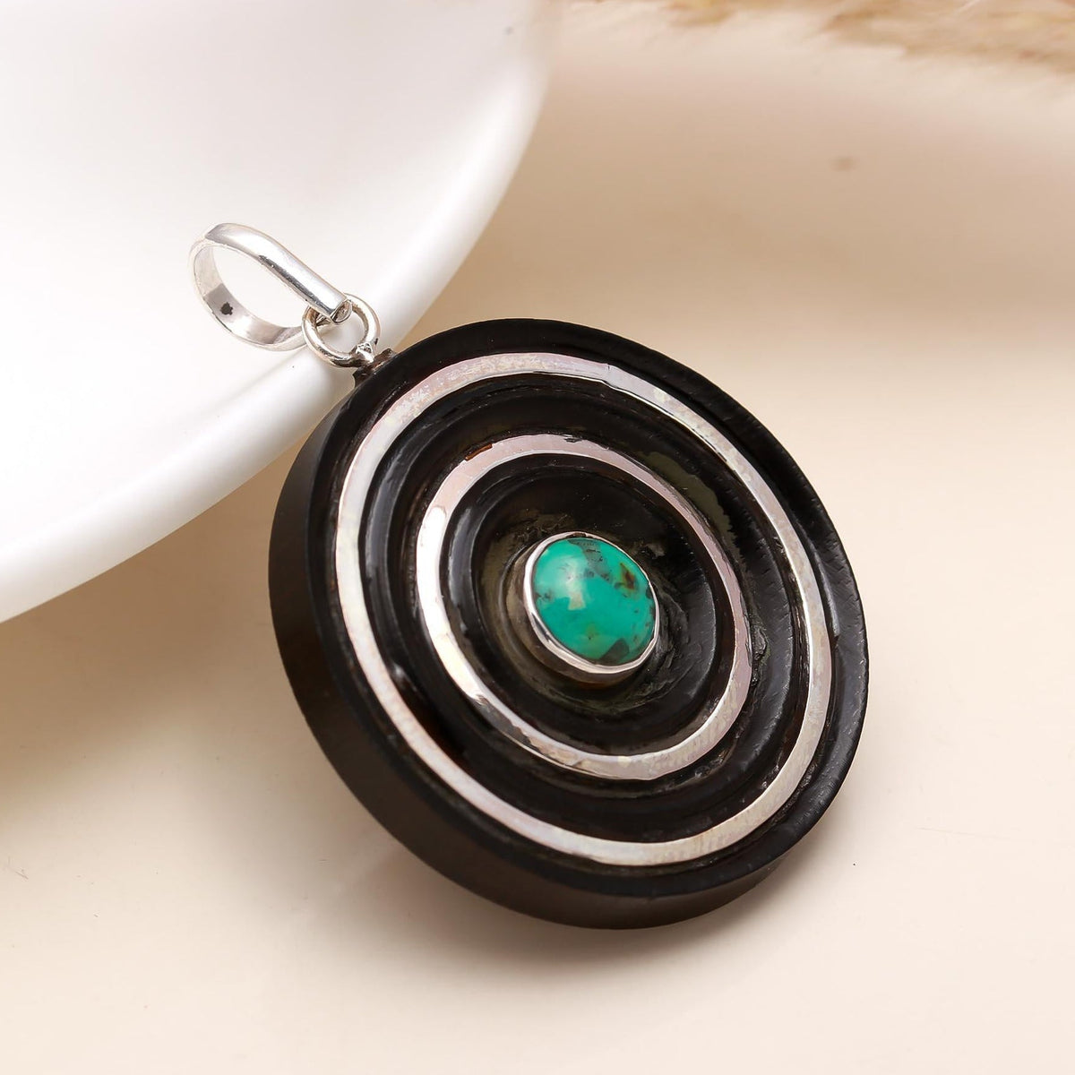 Jewelry pendant with black, white, and turquoise design on a beige surface