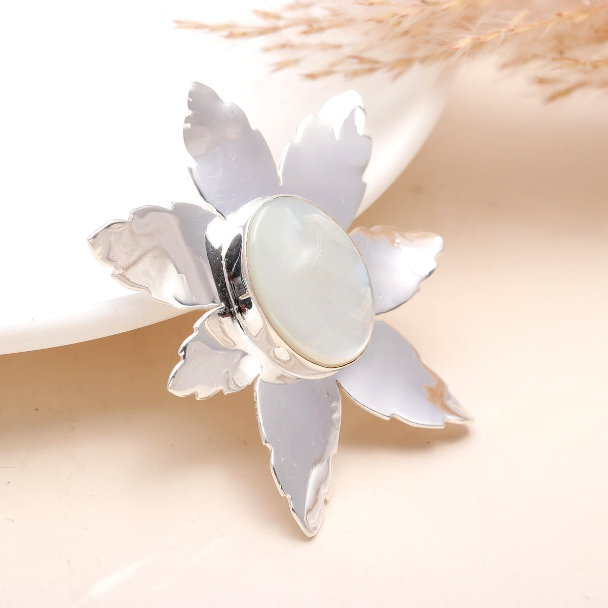 A 925 sterling silver and stone stubbed pendant with a floral design, featuring a central white stone set in a silver frame, presented on a white background with dried plant elements.