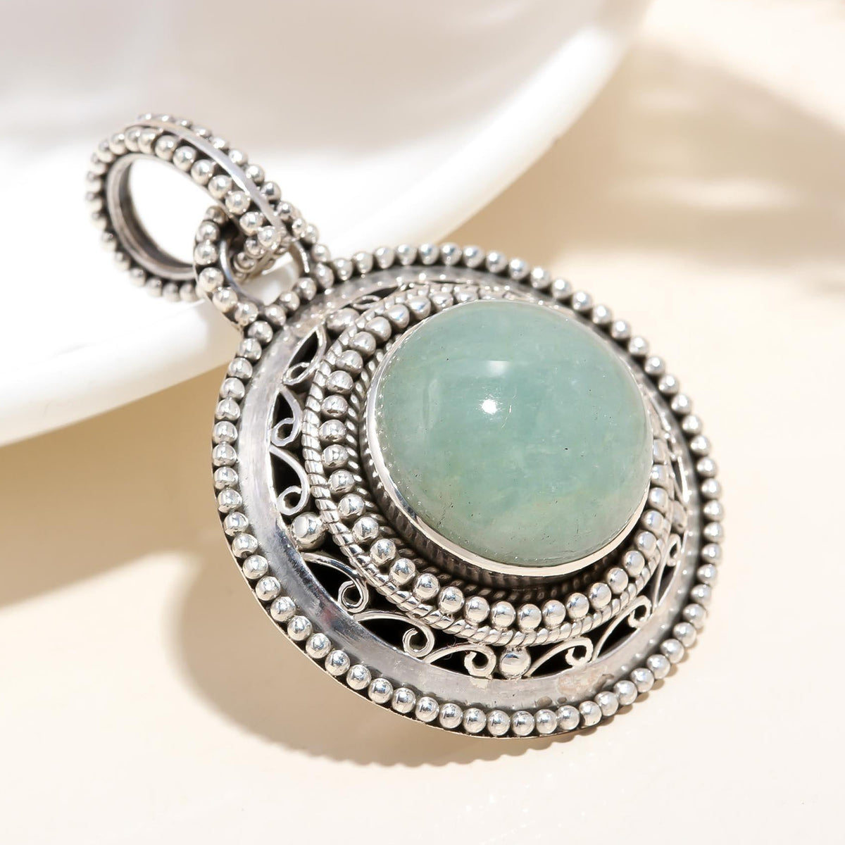 A sterling silver necklace with a filigree pattern and an aquamarine stone circle pendant.