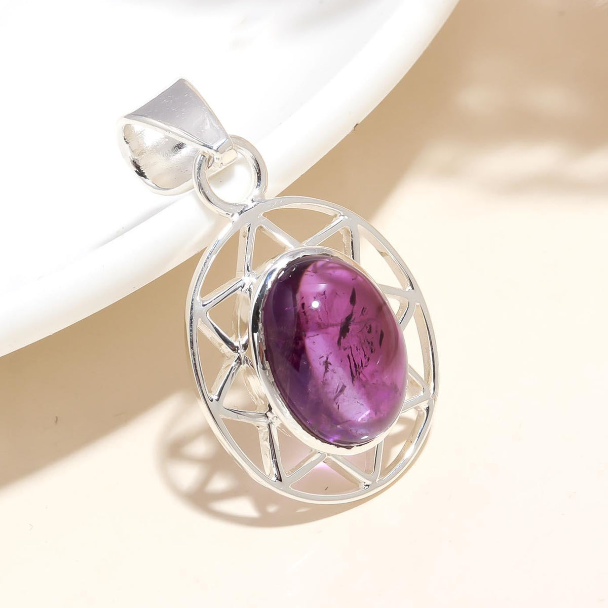 An oval-shaped designer pendant with a deep purple amethyst stone, framed in a sterling silver setting, displayed against a light background.