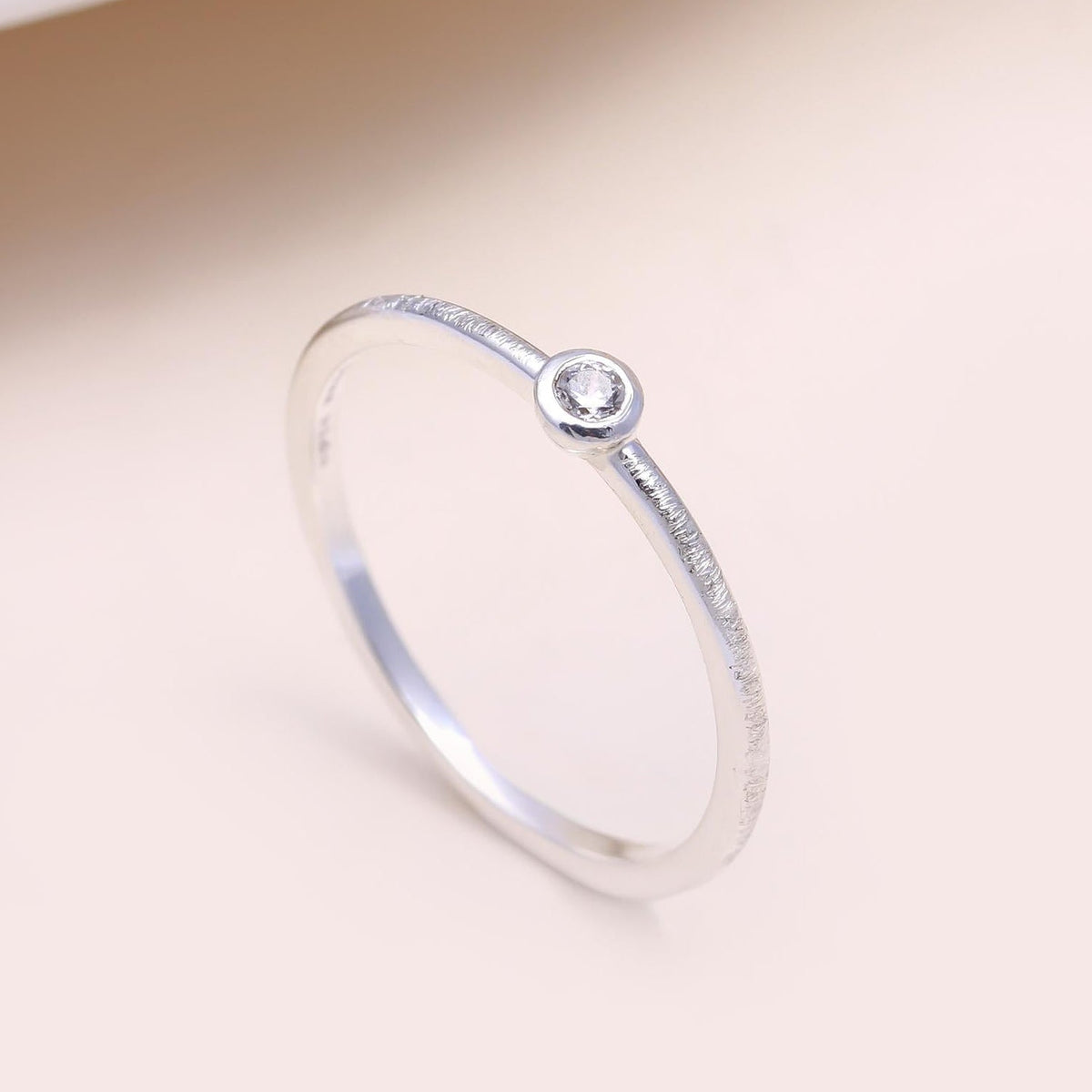 Silver ring with a small diamond on a beige background
