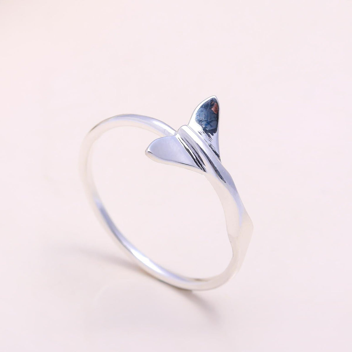 Silver ring with a small shark fin design on a light pink background