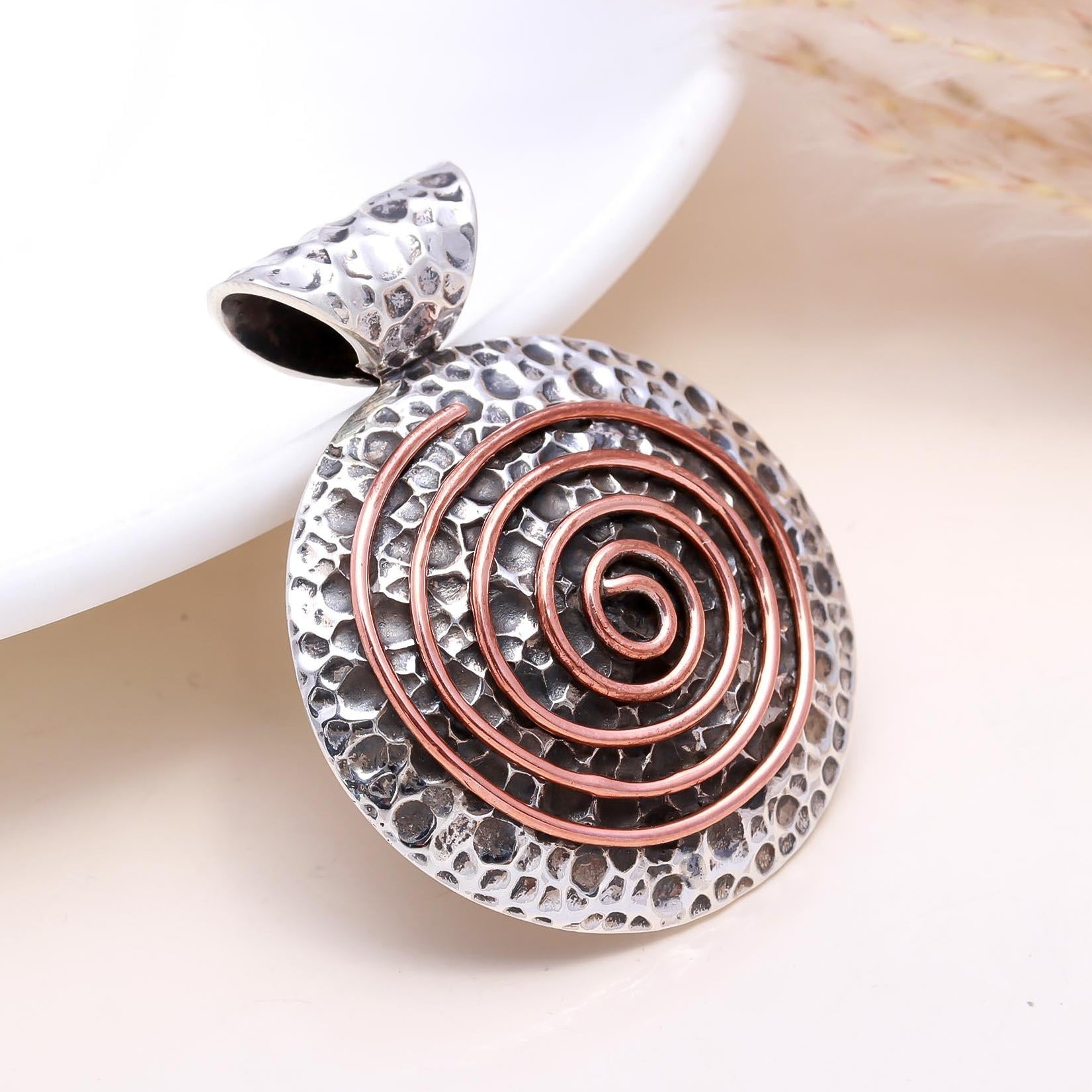 Silver and copper spiral pendant on a light background