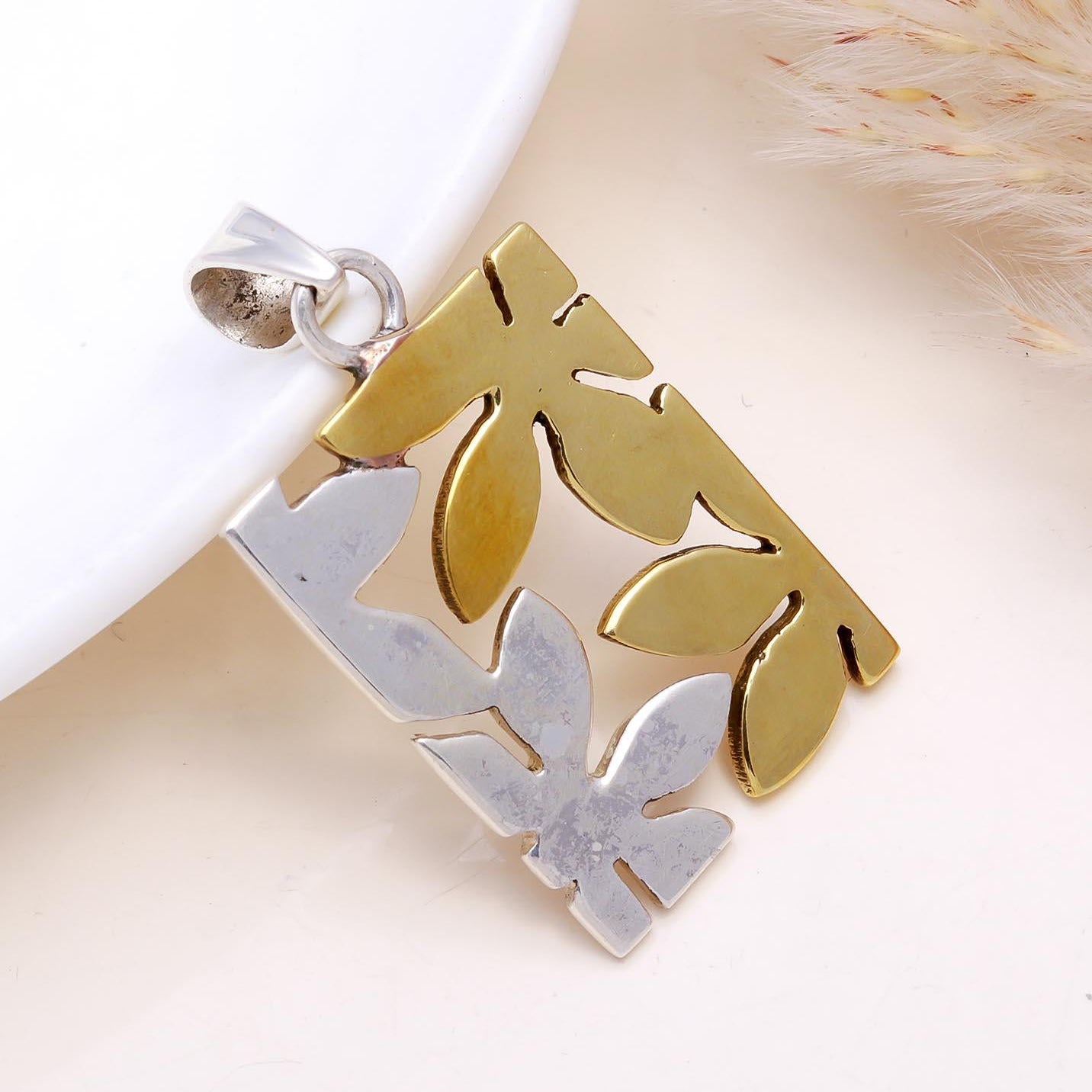 Gold and silver pendant on a white background with dried grass