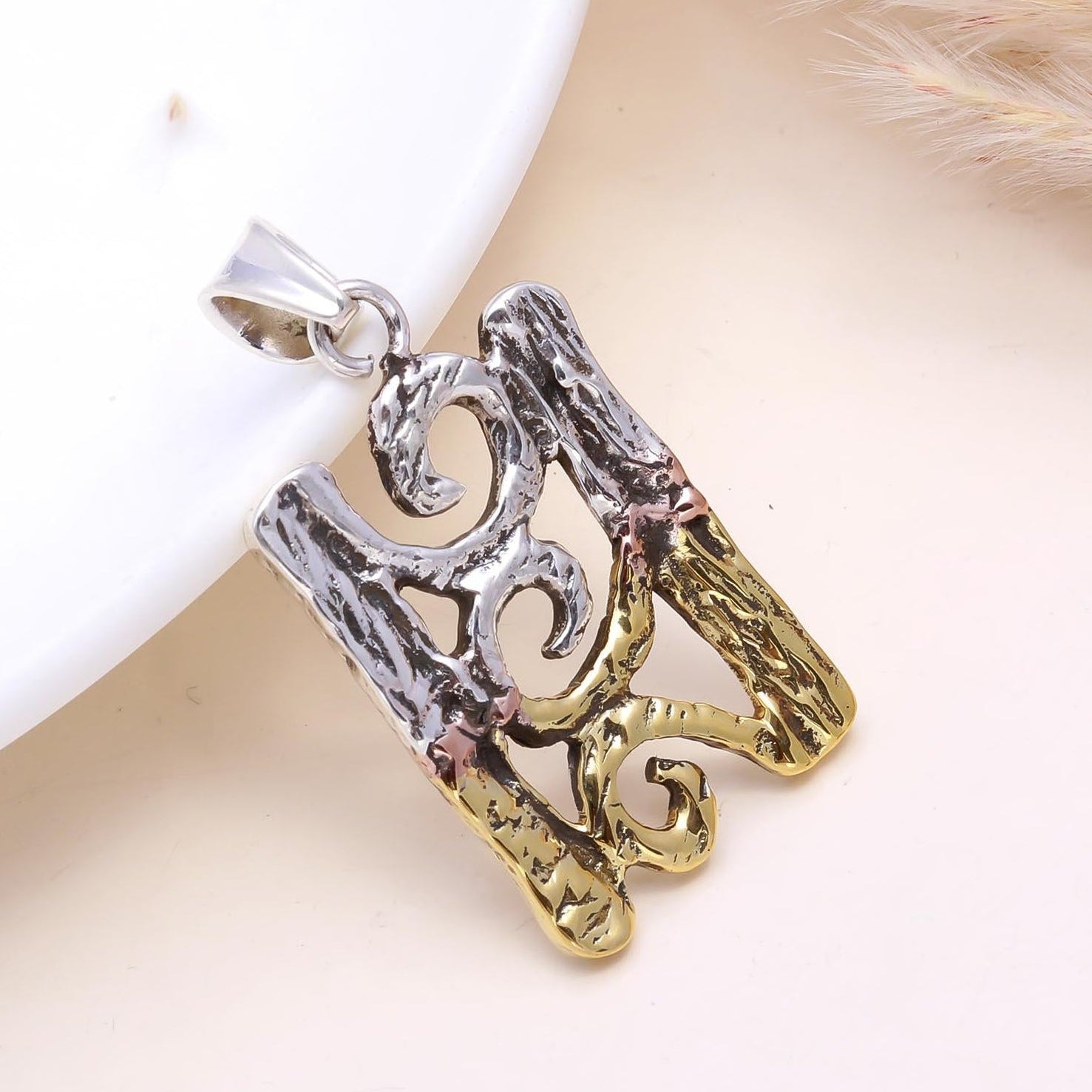 Three metallic pendants in silver, gold, and rose gold on a white surface with a blurred background.
