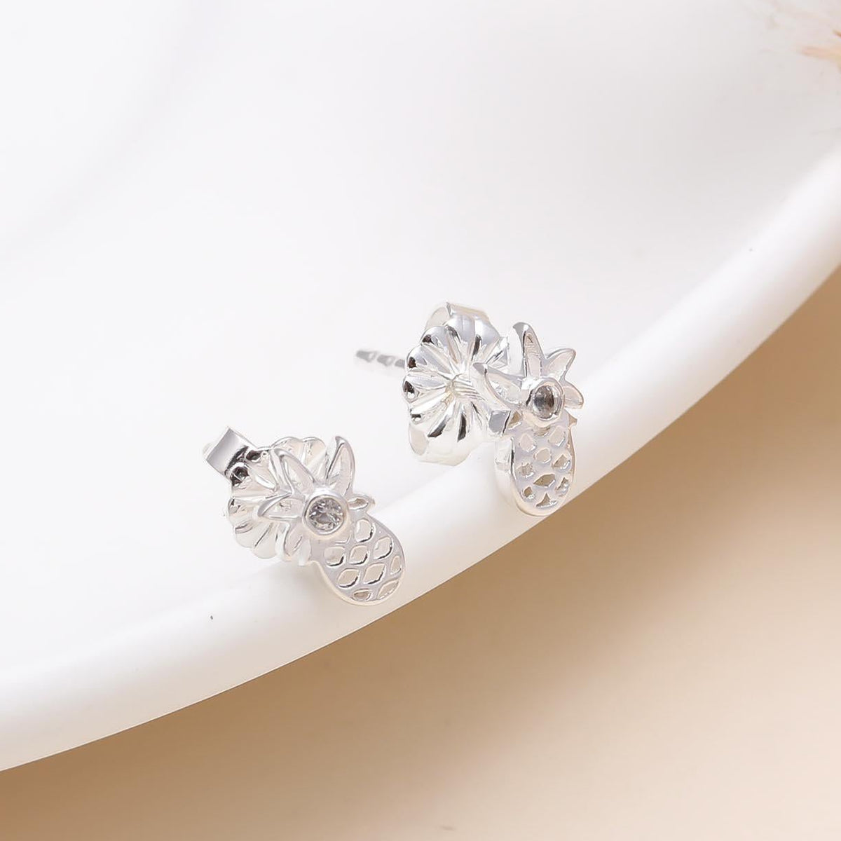 A pair of 925 sterling silver tropical pineapple stud earrings displayed on a white plate, featuring a cute and stylish pineapple shape with a polished finish.