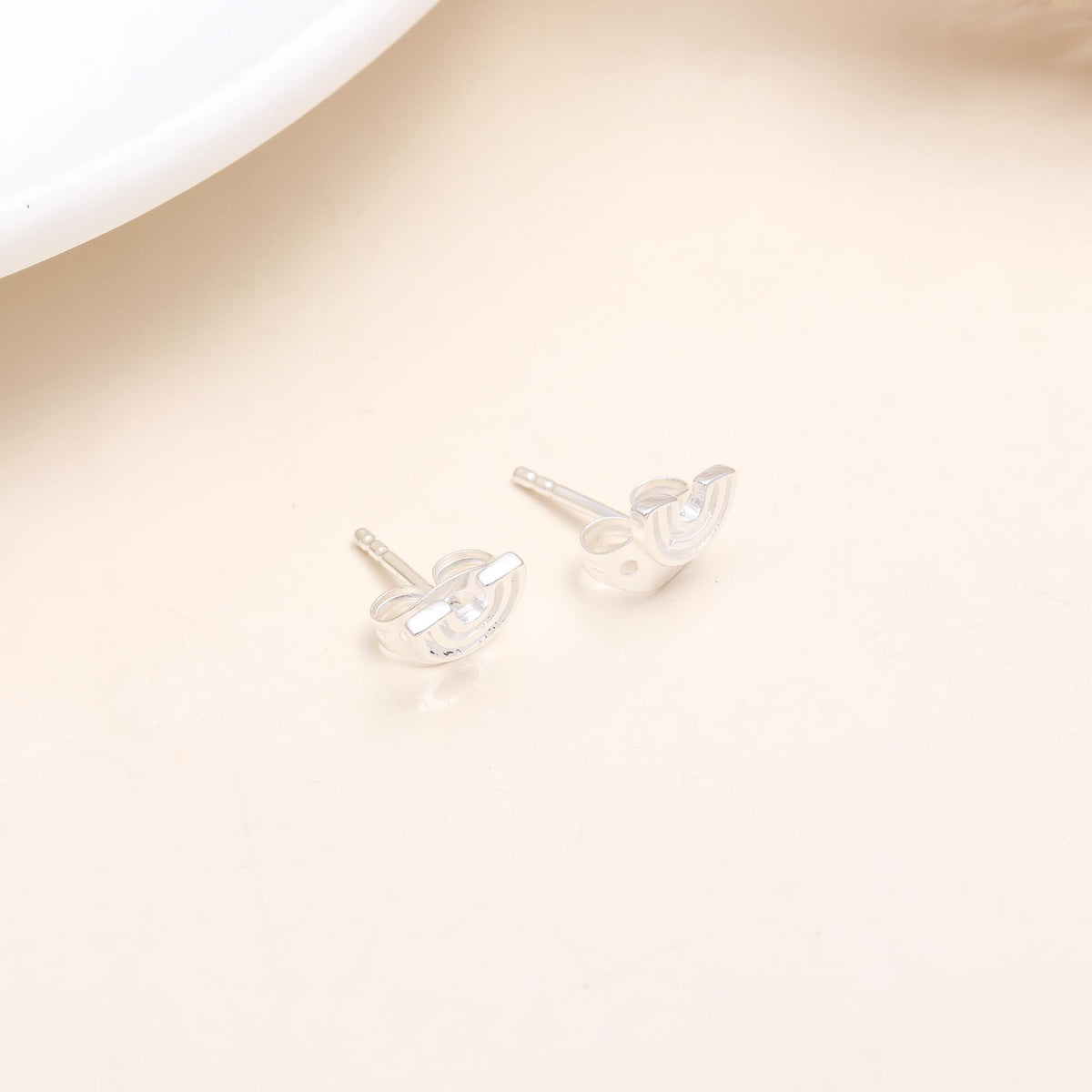 A pair of 925 sterling silver rainbow stud earrings placed on a beige surface.